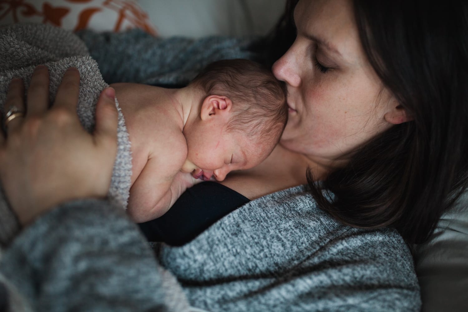 Mom kisses her sleeping newborn's head as they cuddle in bed