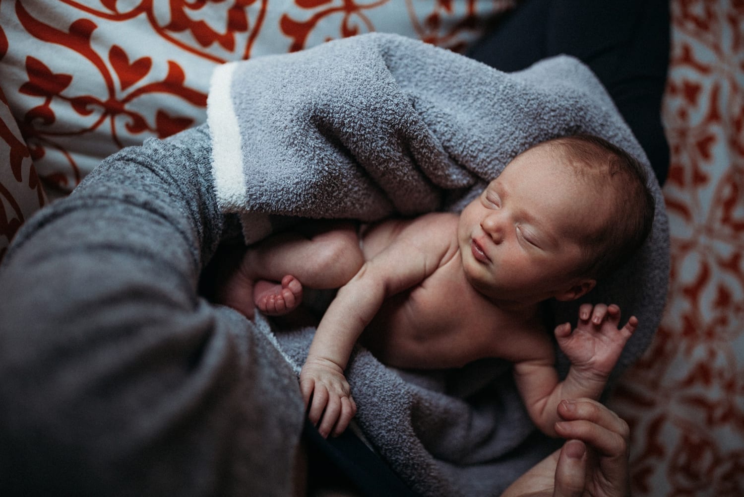 Sleeping newborn wrapped in a gray blanket in a parent's arms, from above