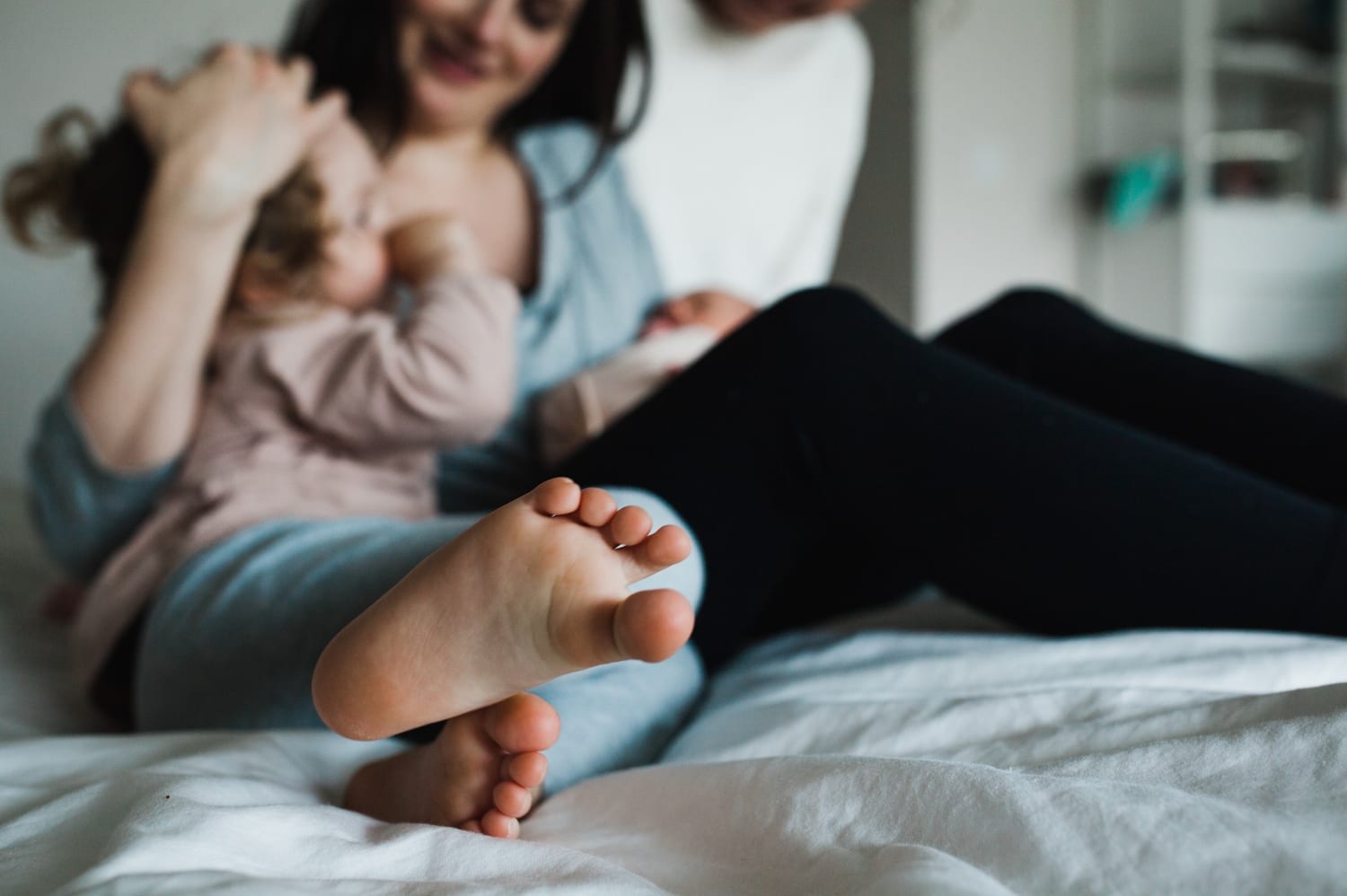 Toddler's bare feet in focus as the family snuggles on the bed behind
