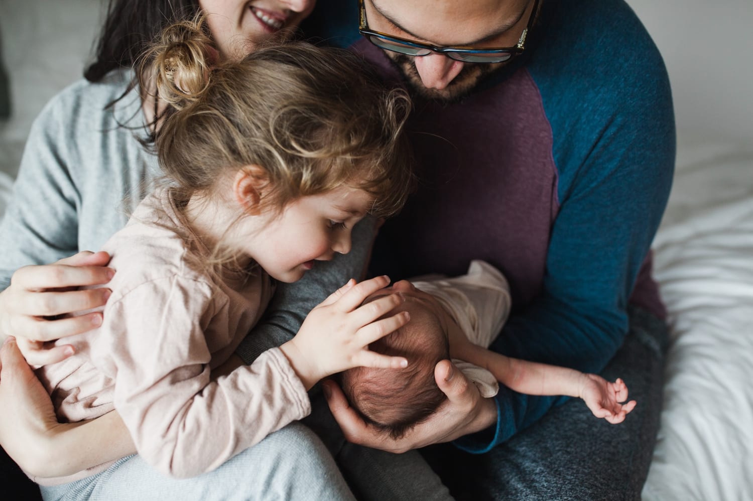 Big sister gently touches the newborn's head while parents hold them close