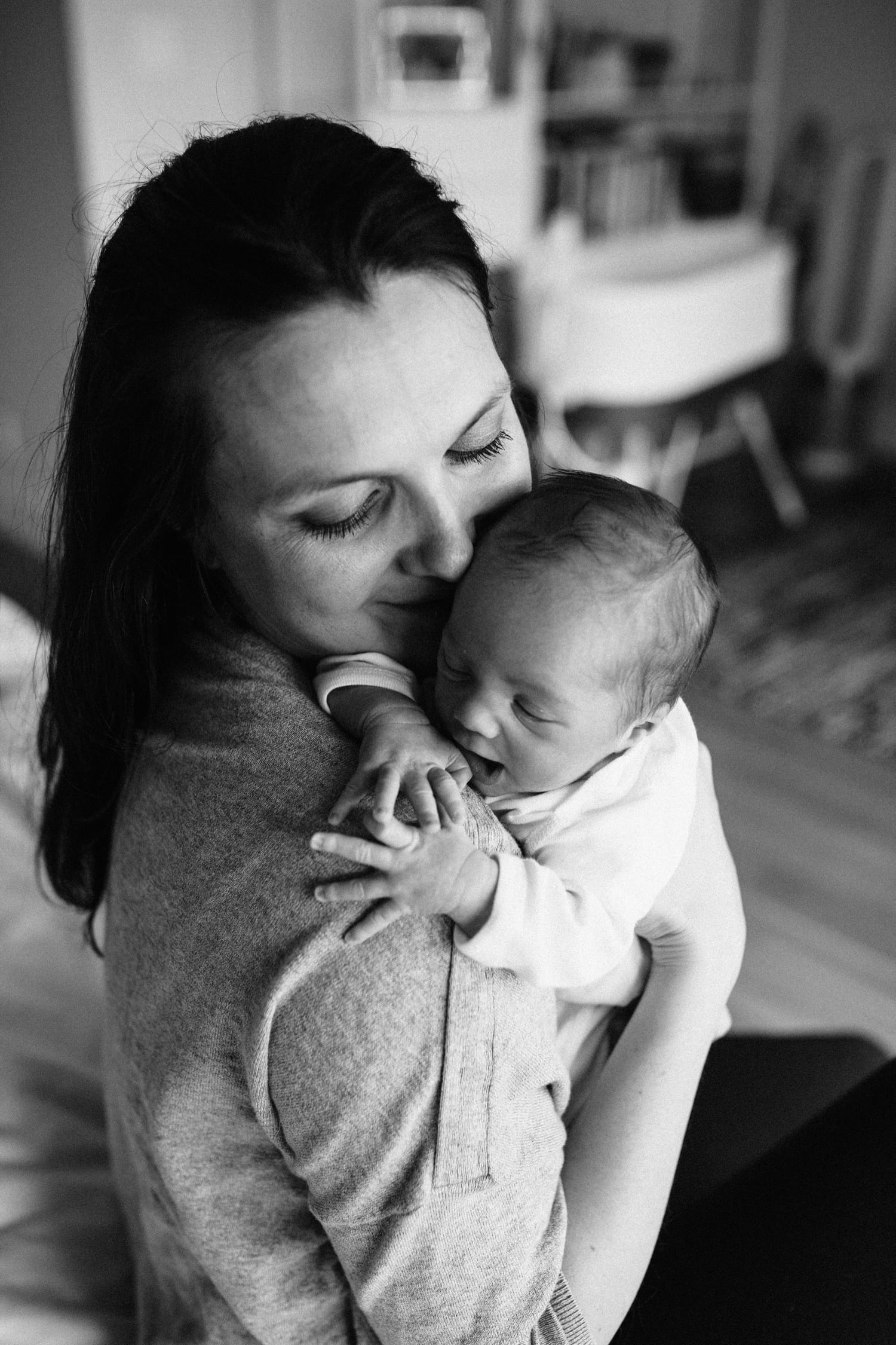 Black and white photo of mom nuzzling her newborn on her shoulder