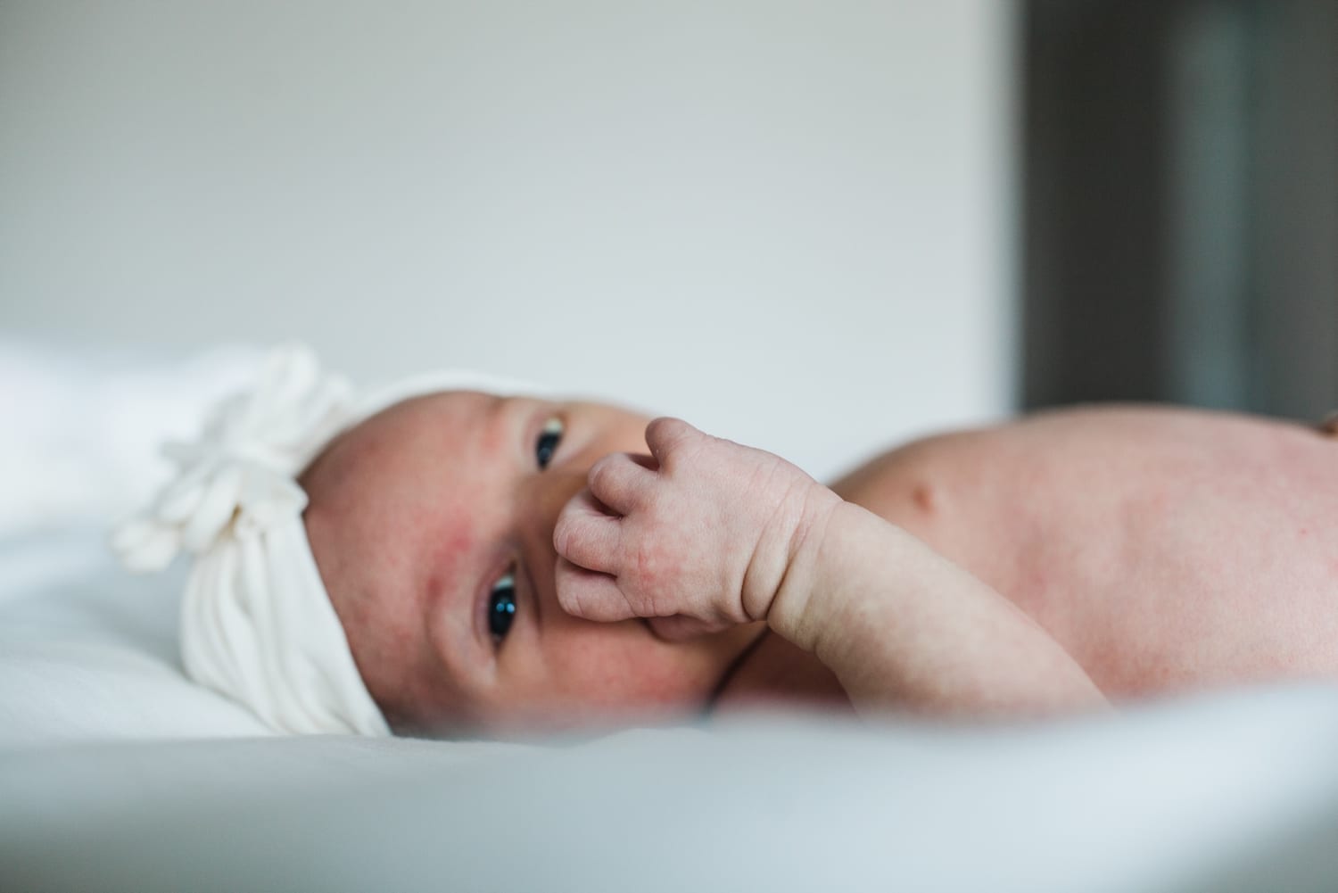 Newborn in a white headband lying on the bed, hand at her cheek