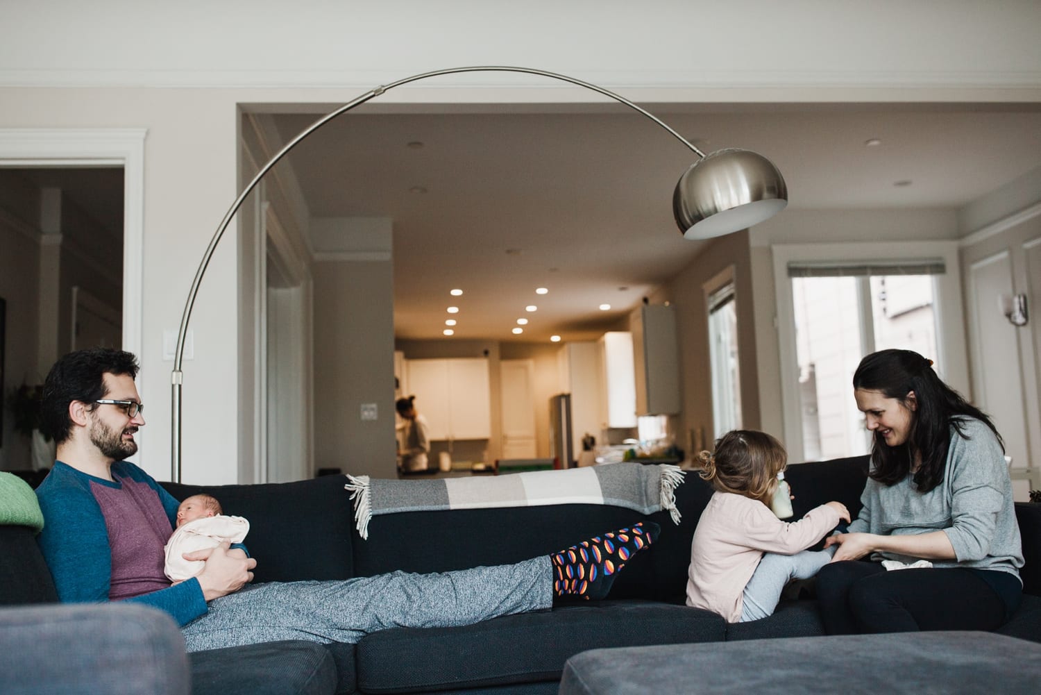 Family relaxing on the couch, dad holding newborn, toddler and mom nearby
