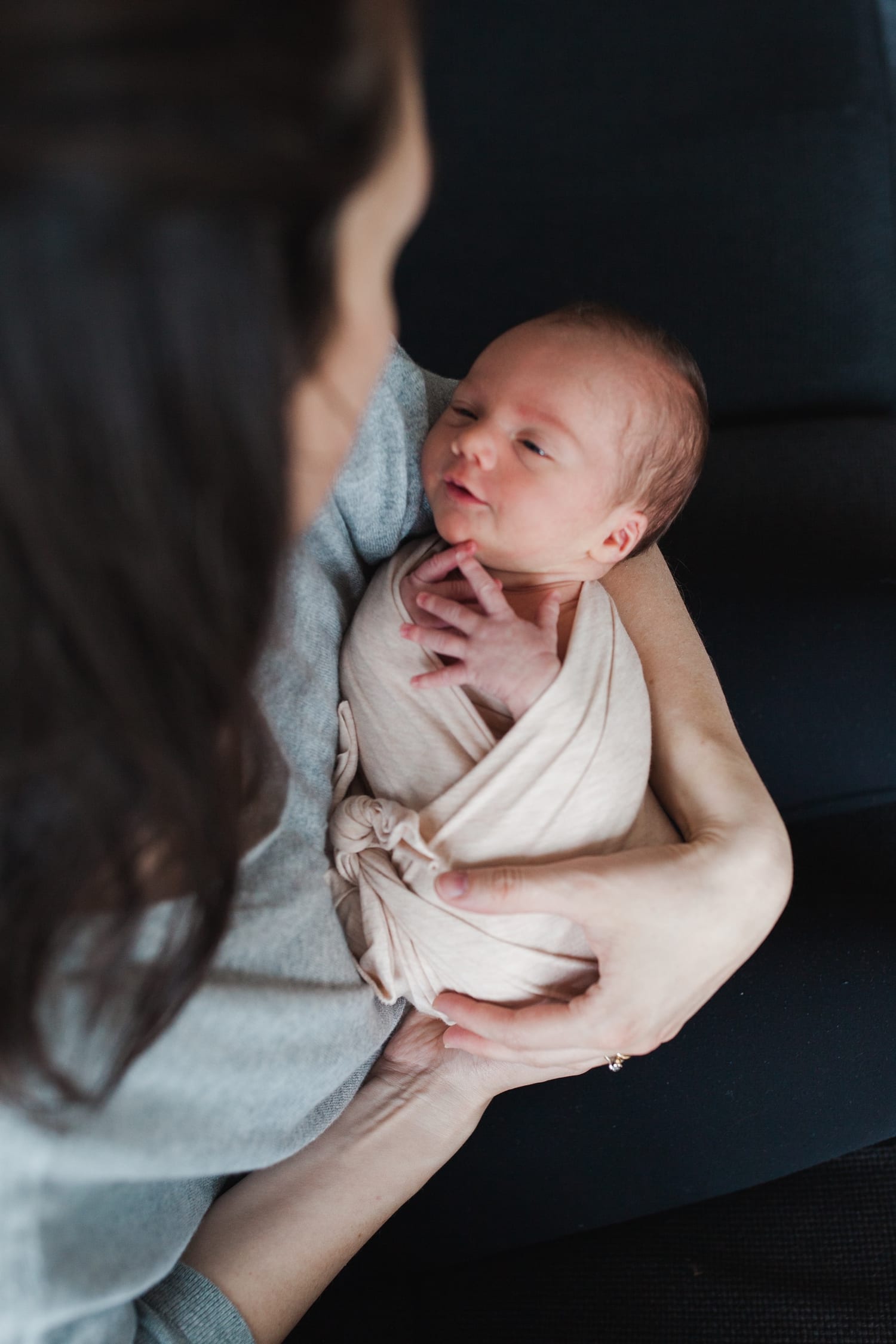 Mom looks down at her awake newborn swaddled in a blush wrap