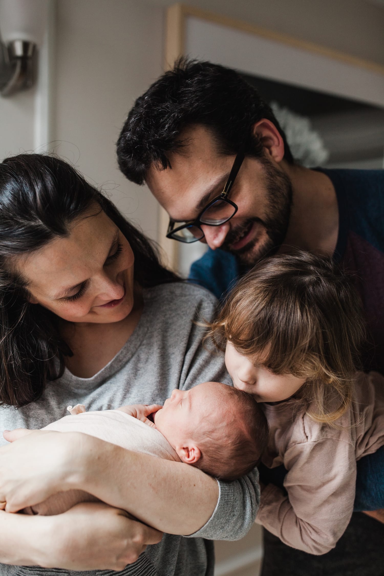 Big sister kisses the newborn's head while mom and dad smile down