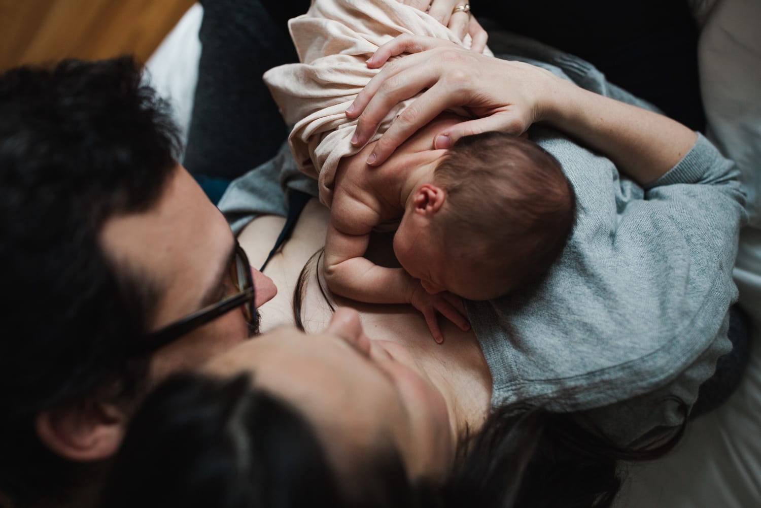 Overhead view of parents snuggling, newborn resting on mom's chest