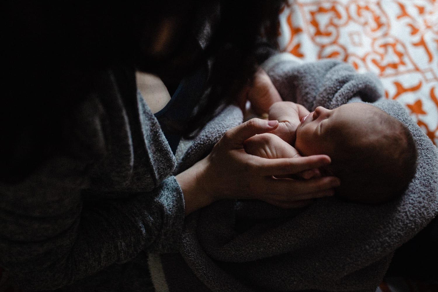 Newborn nestled in mom's hands, wrapped in a cozy blanket in low light