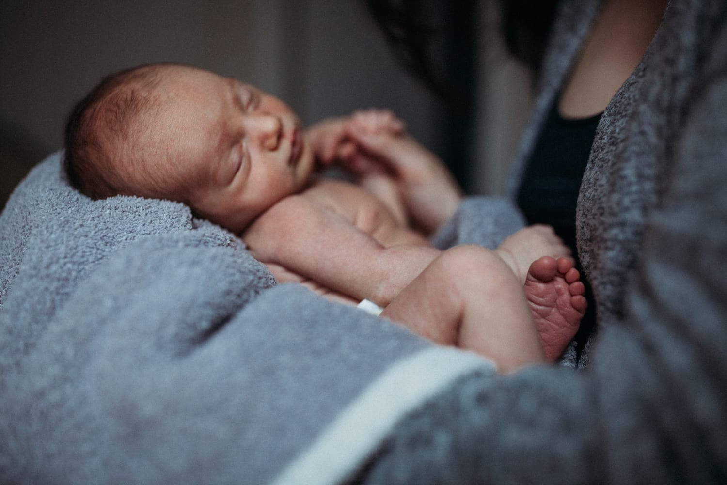Newborn dozing in a gray towel on mom's lap, legs crossed