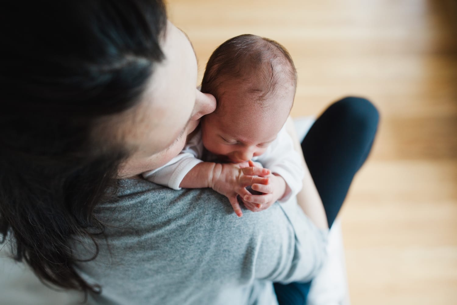 Mom kisses her newborn's head, baby's hands clasped at her shoulder