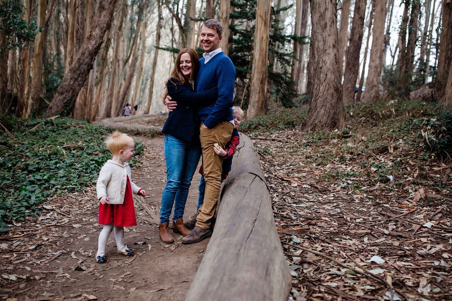 Parents hug beside the wood line log while their two kids play nearby