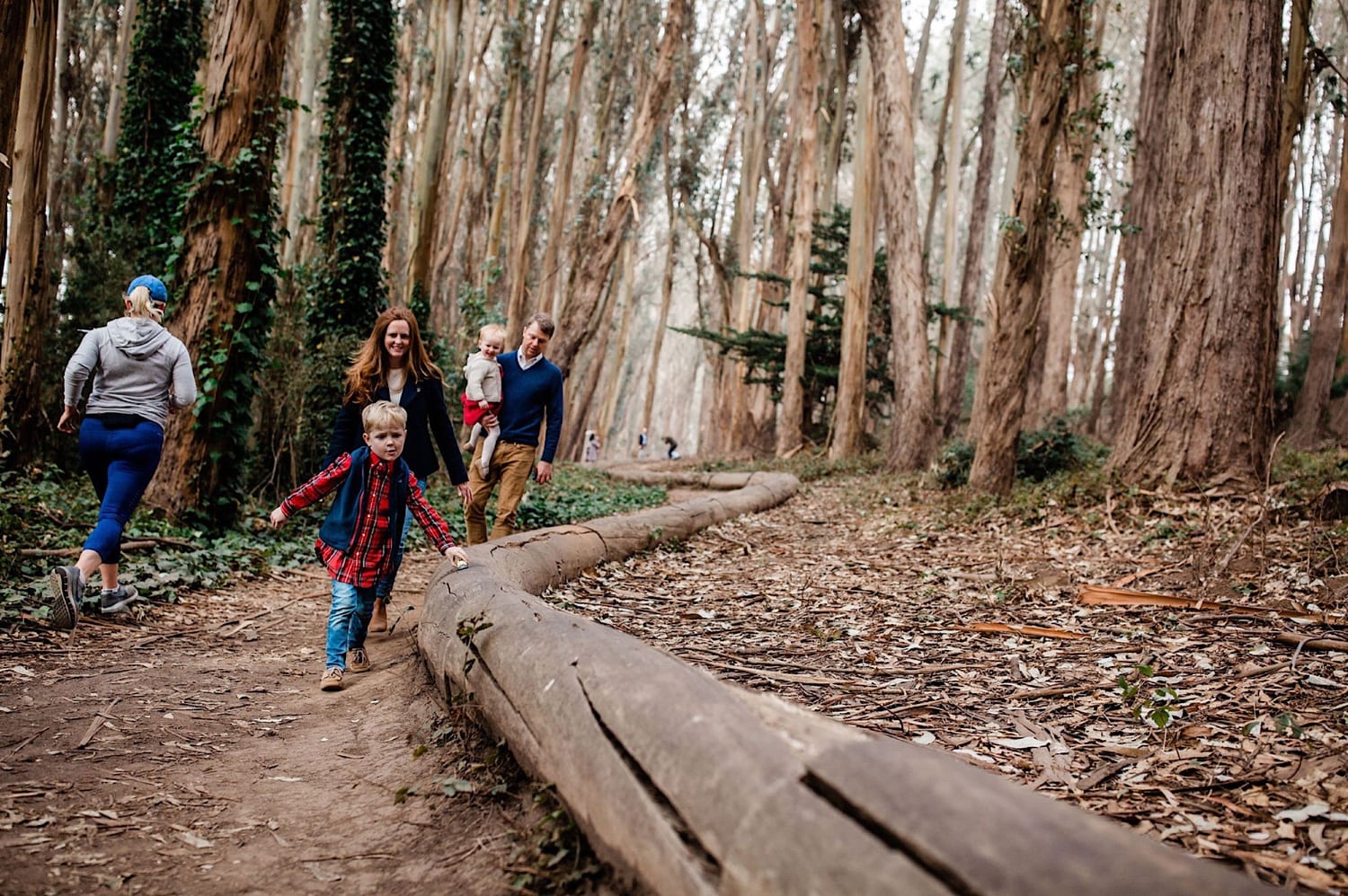 Boy runs ahead along the log as family follows through eucalyptus grove