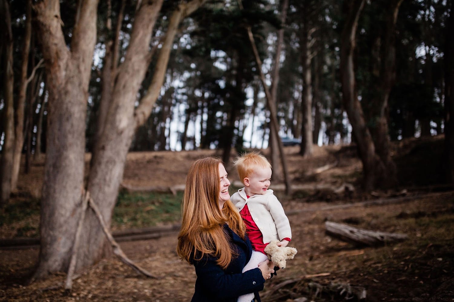 Mom and toddler walk the grove; boy smiles beside green cypress boughs