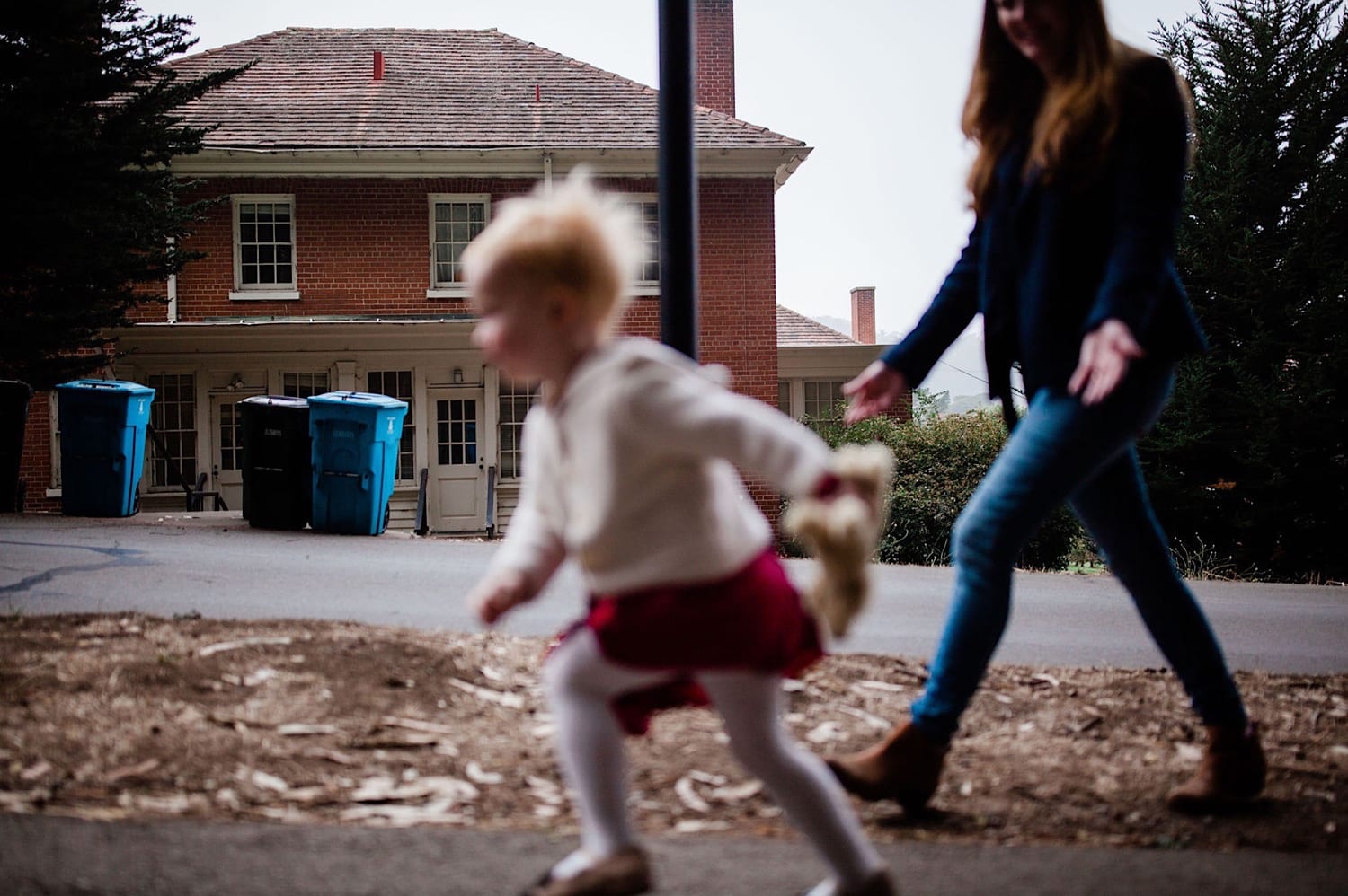 Toddler runs along a path ahead of mom near historic Presidio brick buildings
