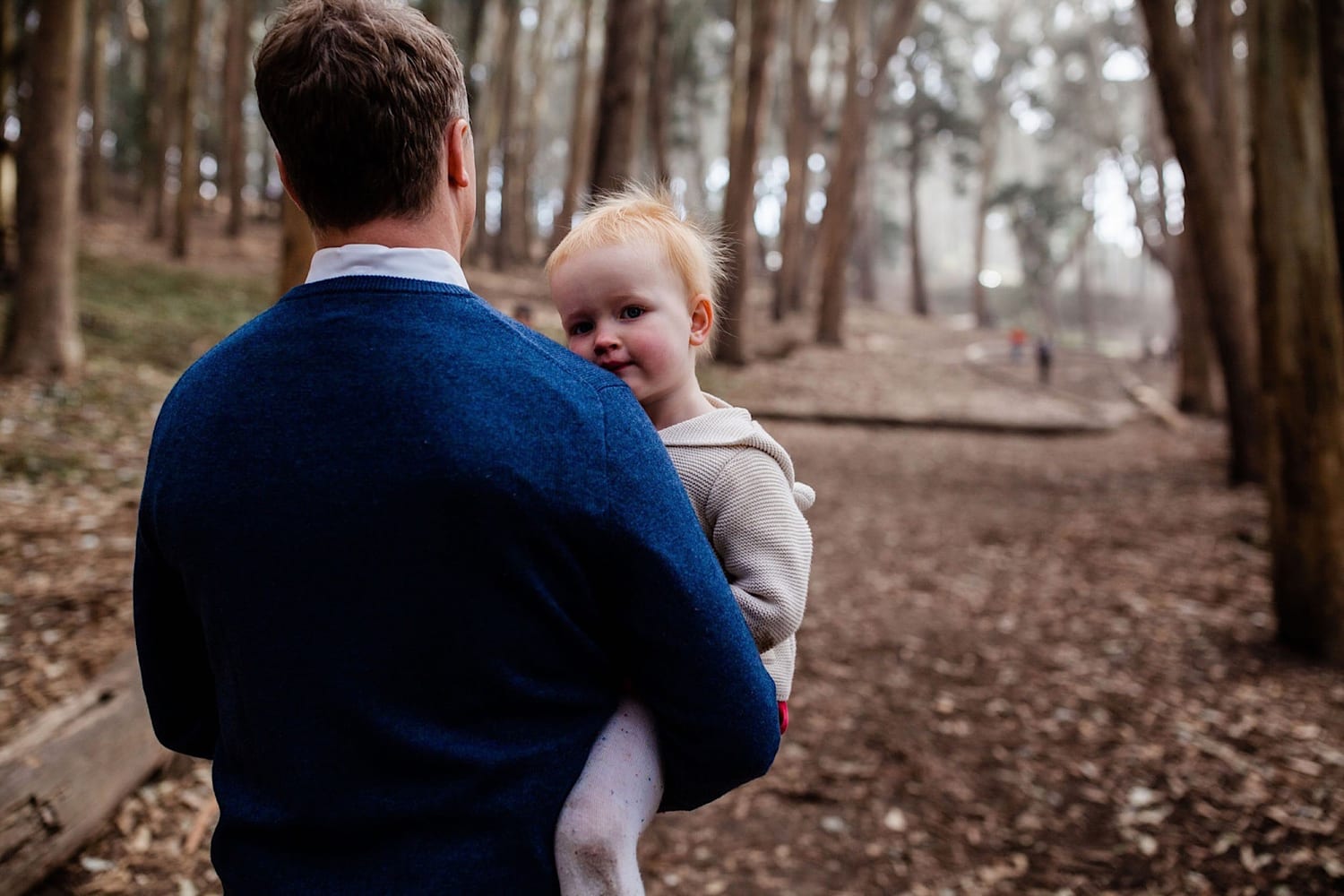 Toddler peers over dad's shoulder as he carries her along the foggy trail
