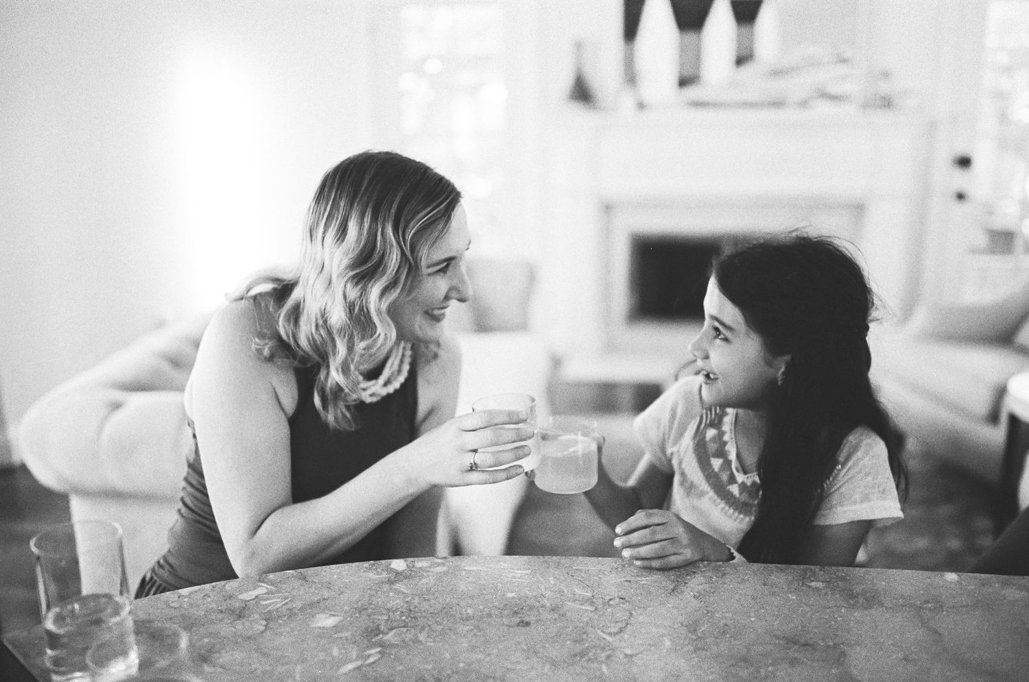 Black and white photo of a mother and daughter clinking glasses at a kitchen counter