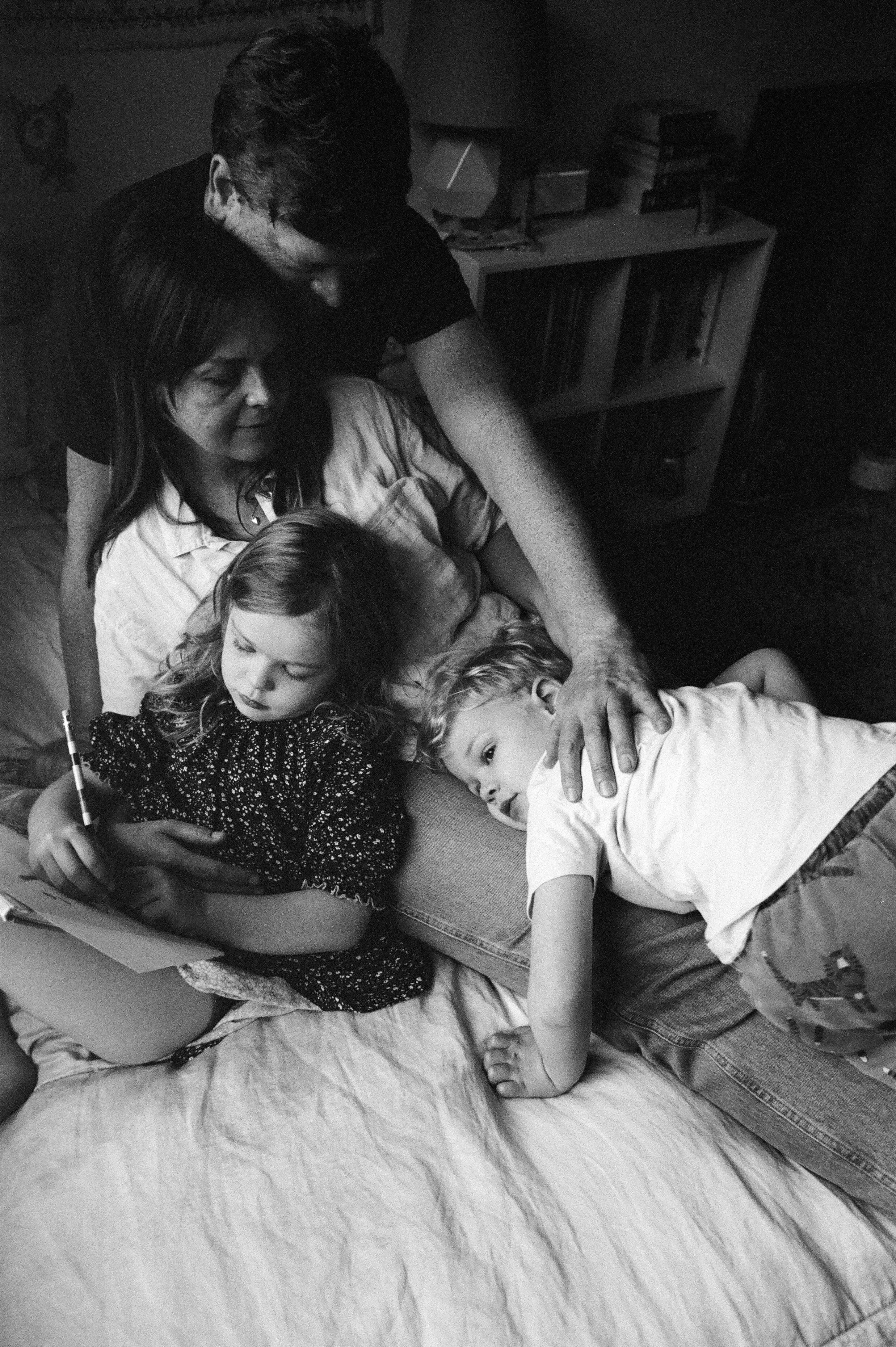 Black and white — family of four together on a bed, quiet in-home lifestyle moment