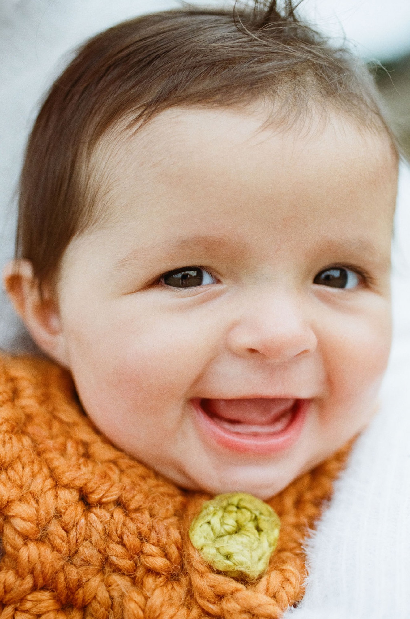 Laughing toddler in orange knit sweater with green button, bright cheerful expression and direct gaze