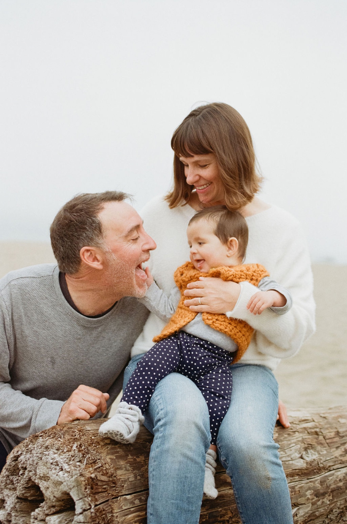 A man playfully pretends to eat a pretzel held by a young boy while a woman smiles beside them on a sandy beach
