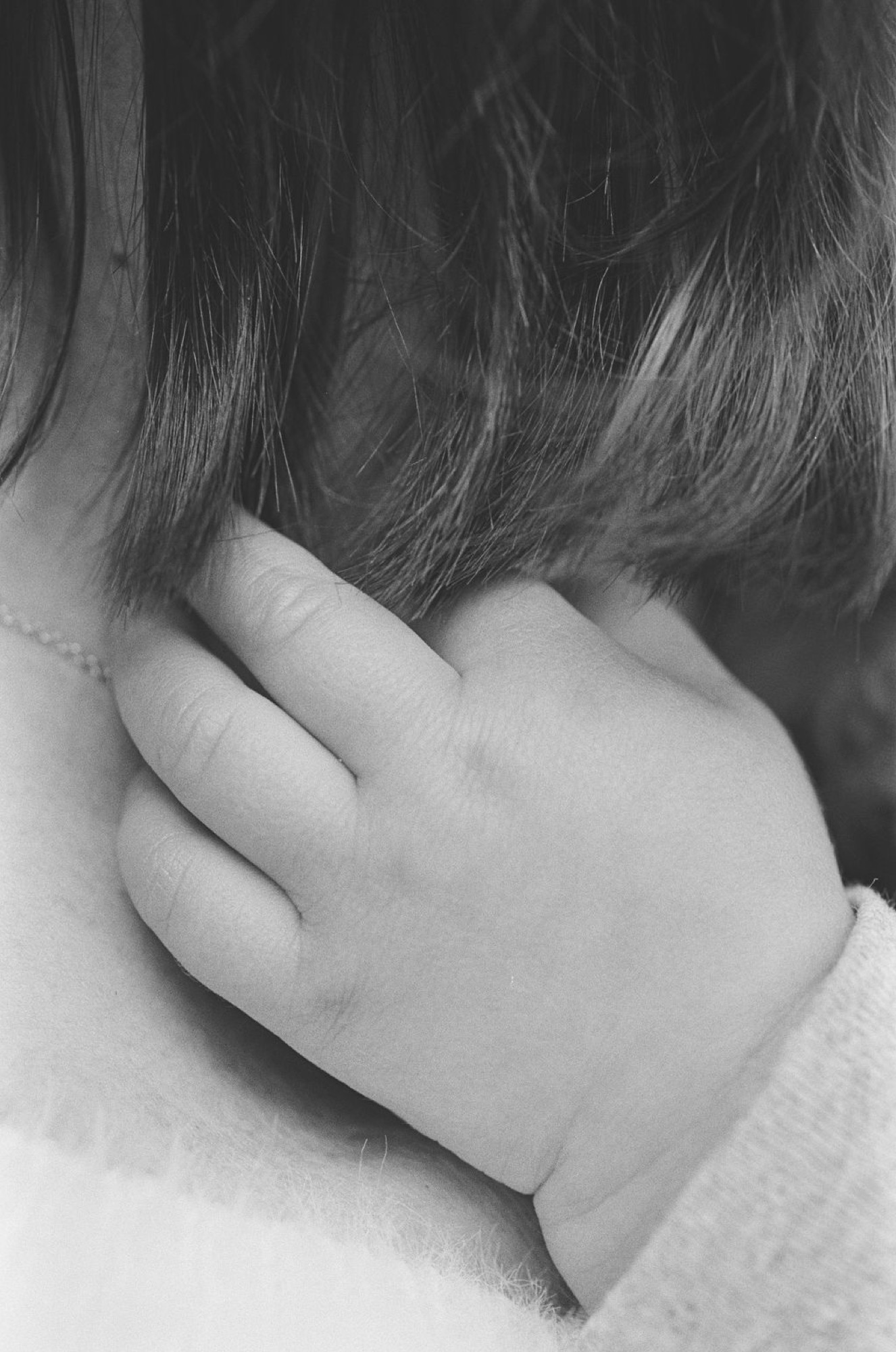 A tender close-up of a small child's hand grasping an adult's shoulder, captured in soft black and white