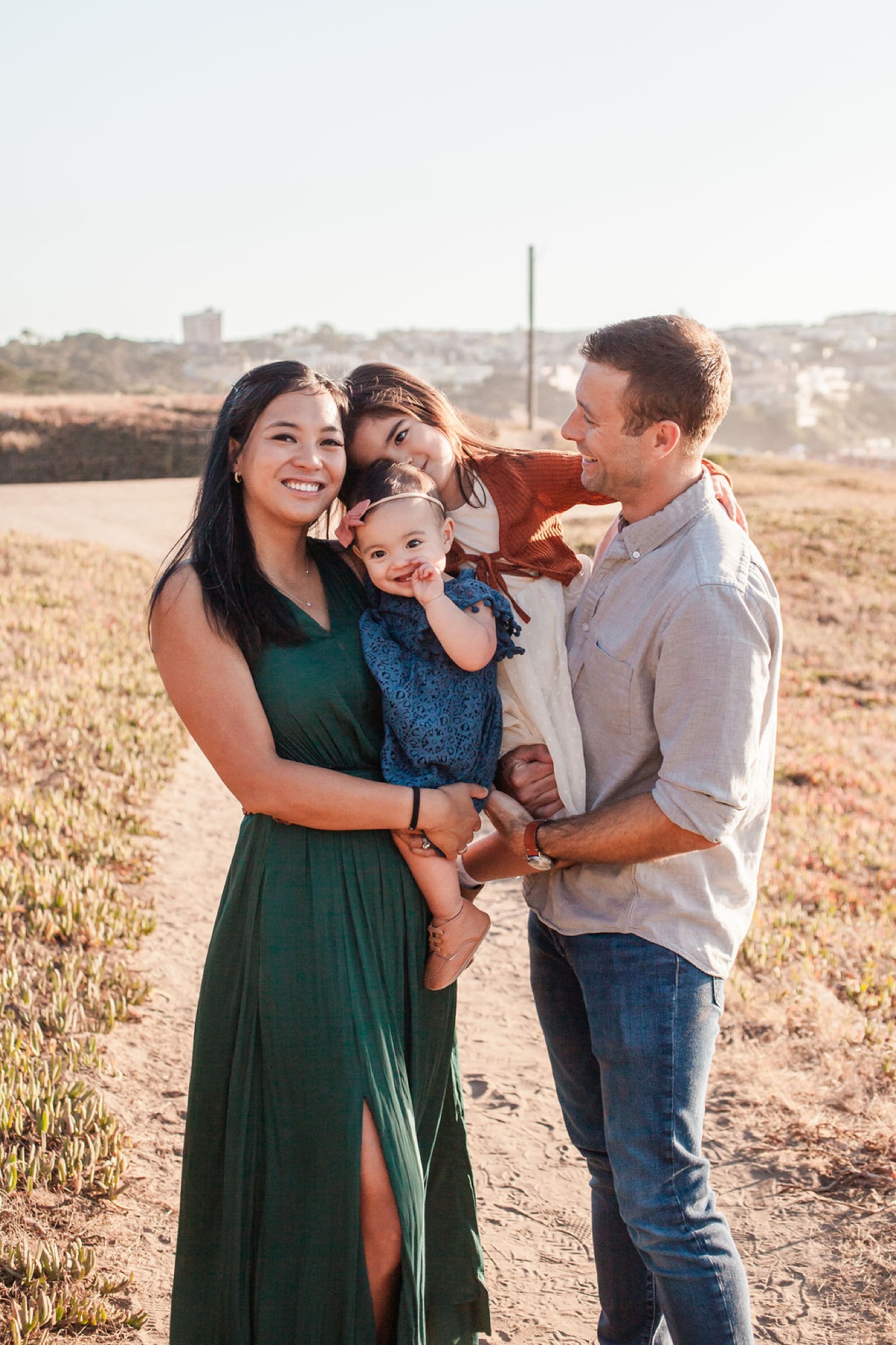 A family of four shares a warm moment in an open field at golden hour, with genuine smiles and relaxed postures suggesting genuine connection
