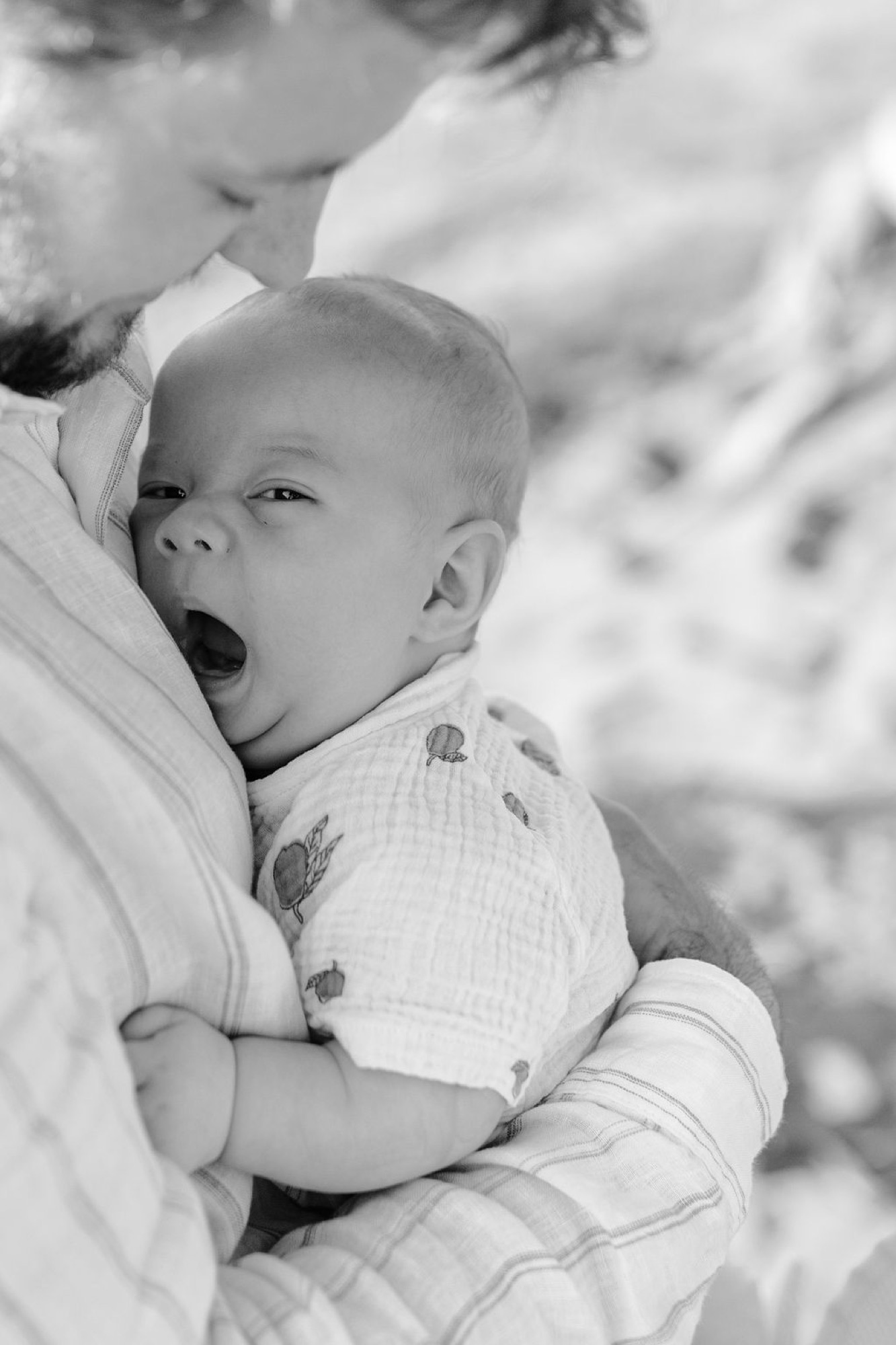 A father holds his yawning infant close to his shoulder in soft natural light, both relaxed and intimate