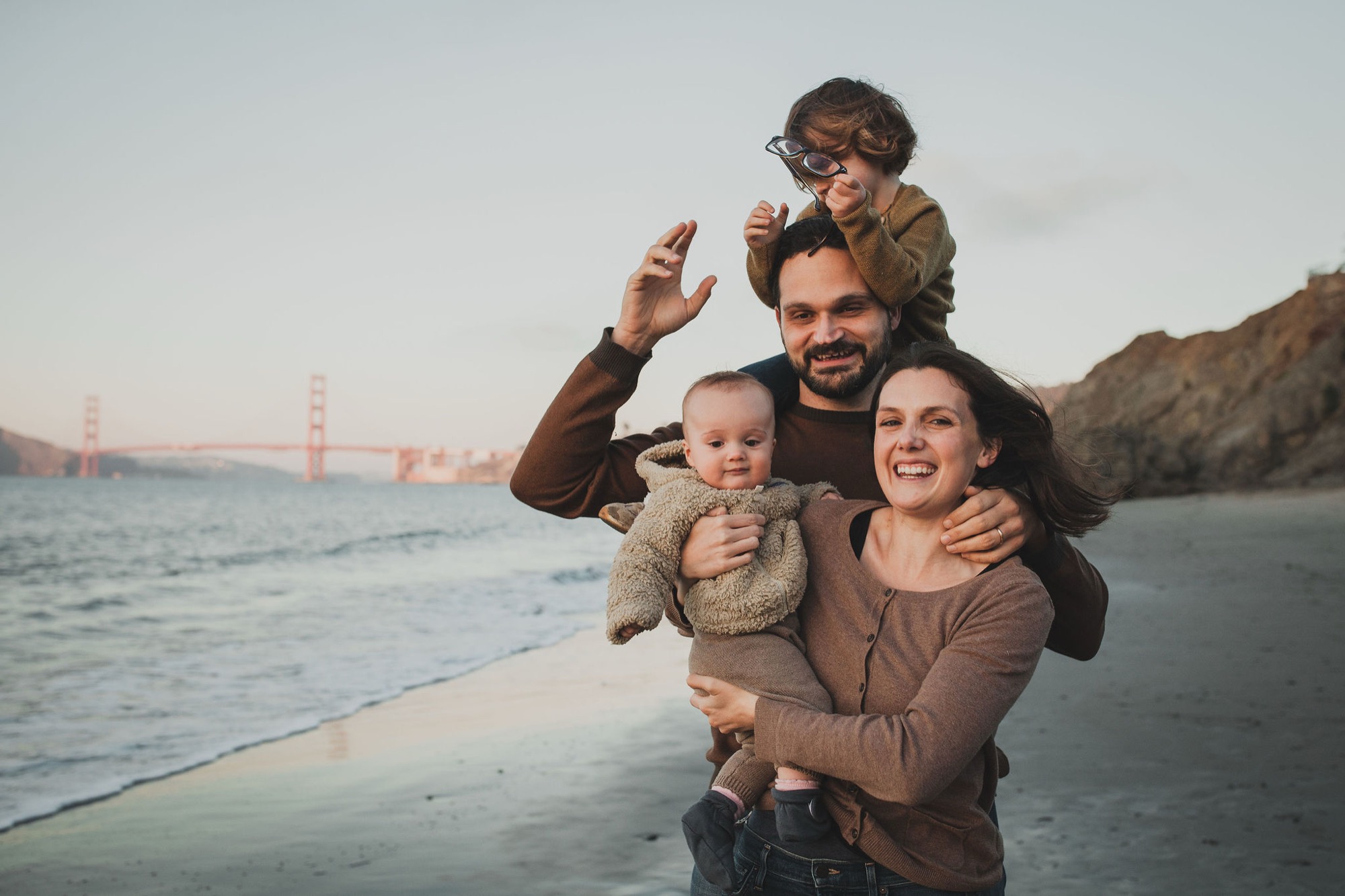 Family of four poses on China Beach with the Golden Gate Bridge glowing in warm sunset light behind them