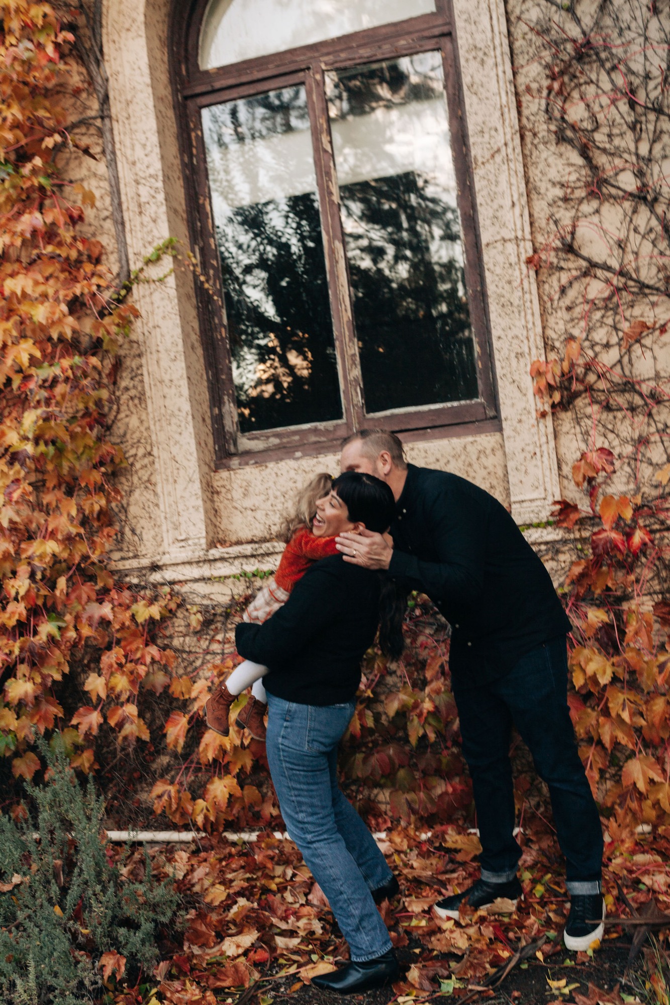 Two figures embrace against an ivy-covered stone wall beneath a weathered window in autumn light