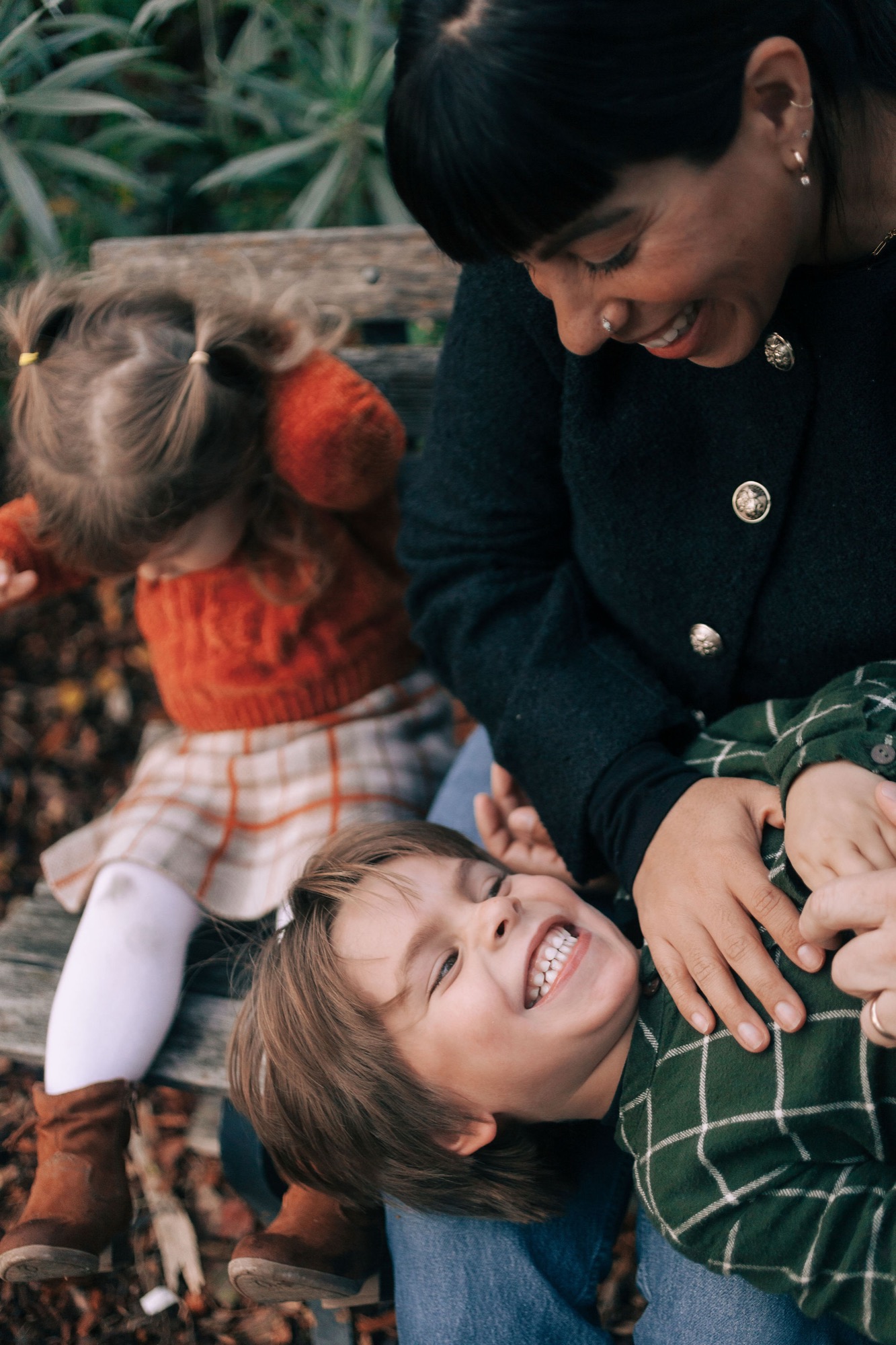 Woman and young child laugh together outdoors, child tilted back in joy while holding a Sesame Street doll in natural afternoon light