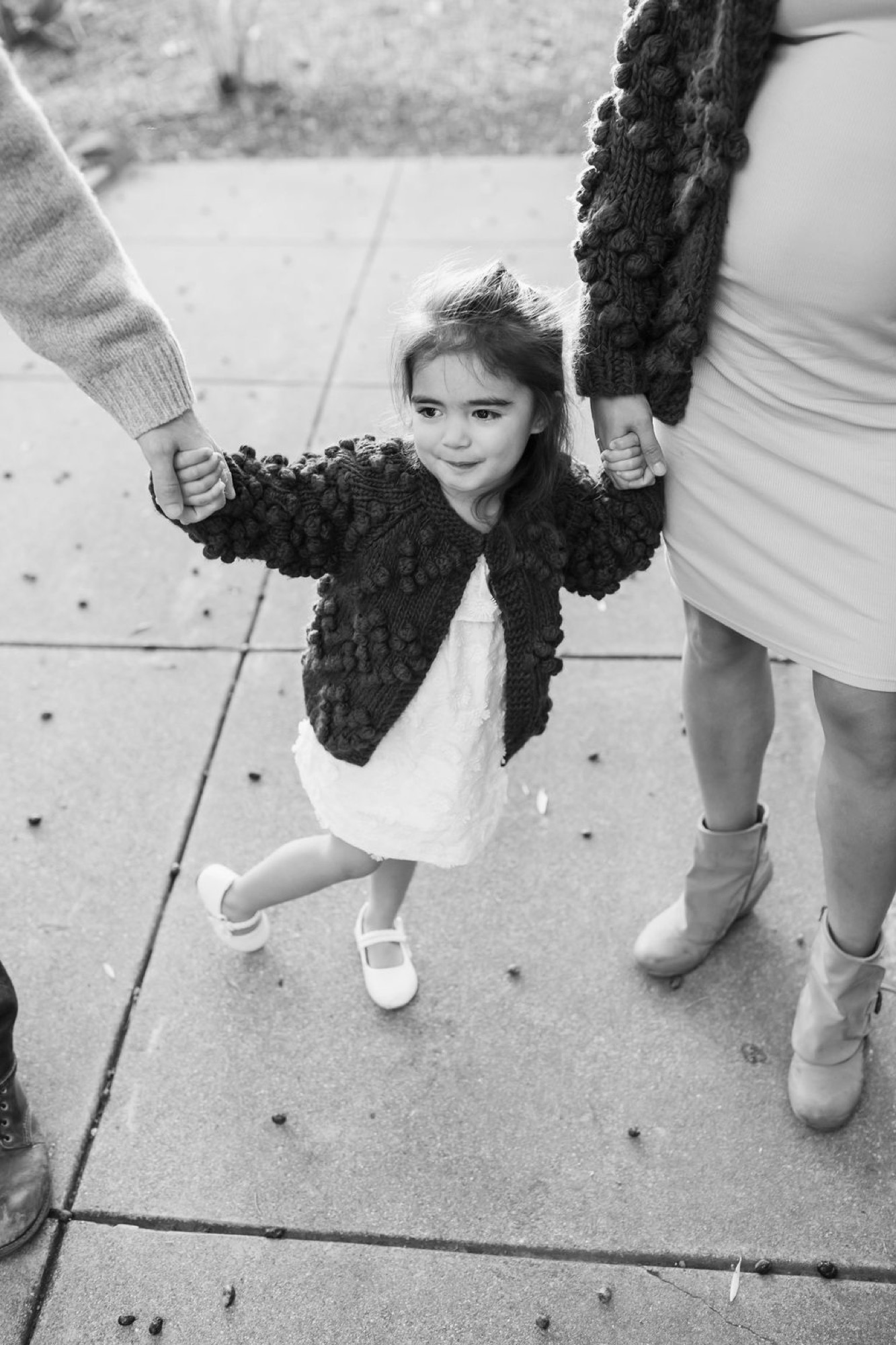 A young child grins while swinging between two adults on a sidewalk, their feet lifted off the concrete in mid-air — San Anselmo Family Photographer