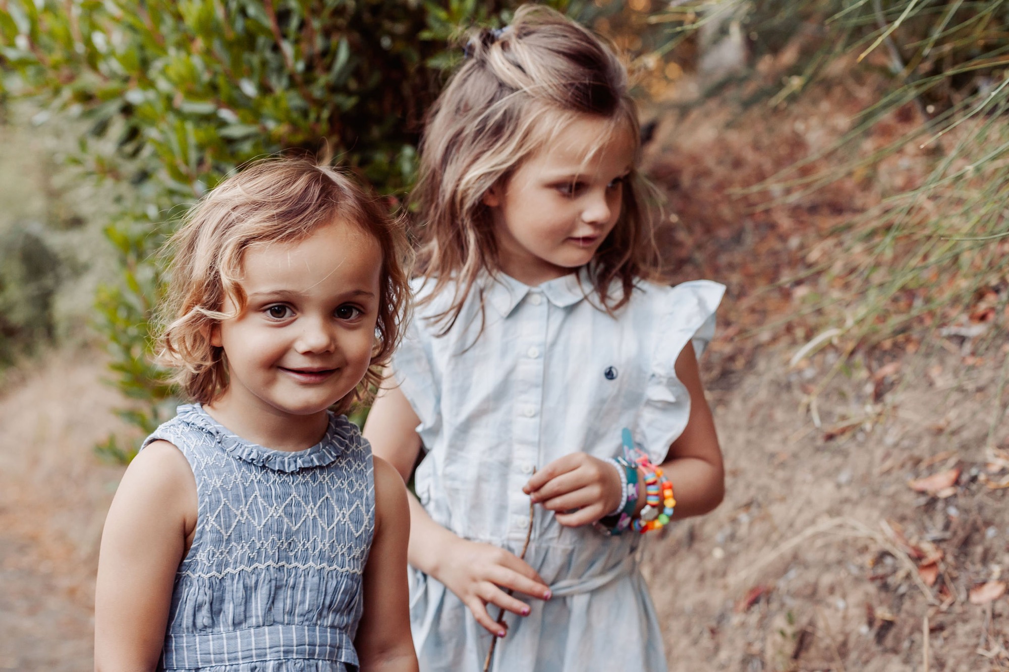 Two young girls stand on a dusty trail, the younger smiling directly at the camera while her older sister gazes thoughtfully aside