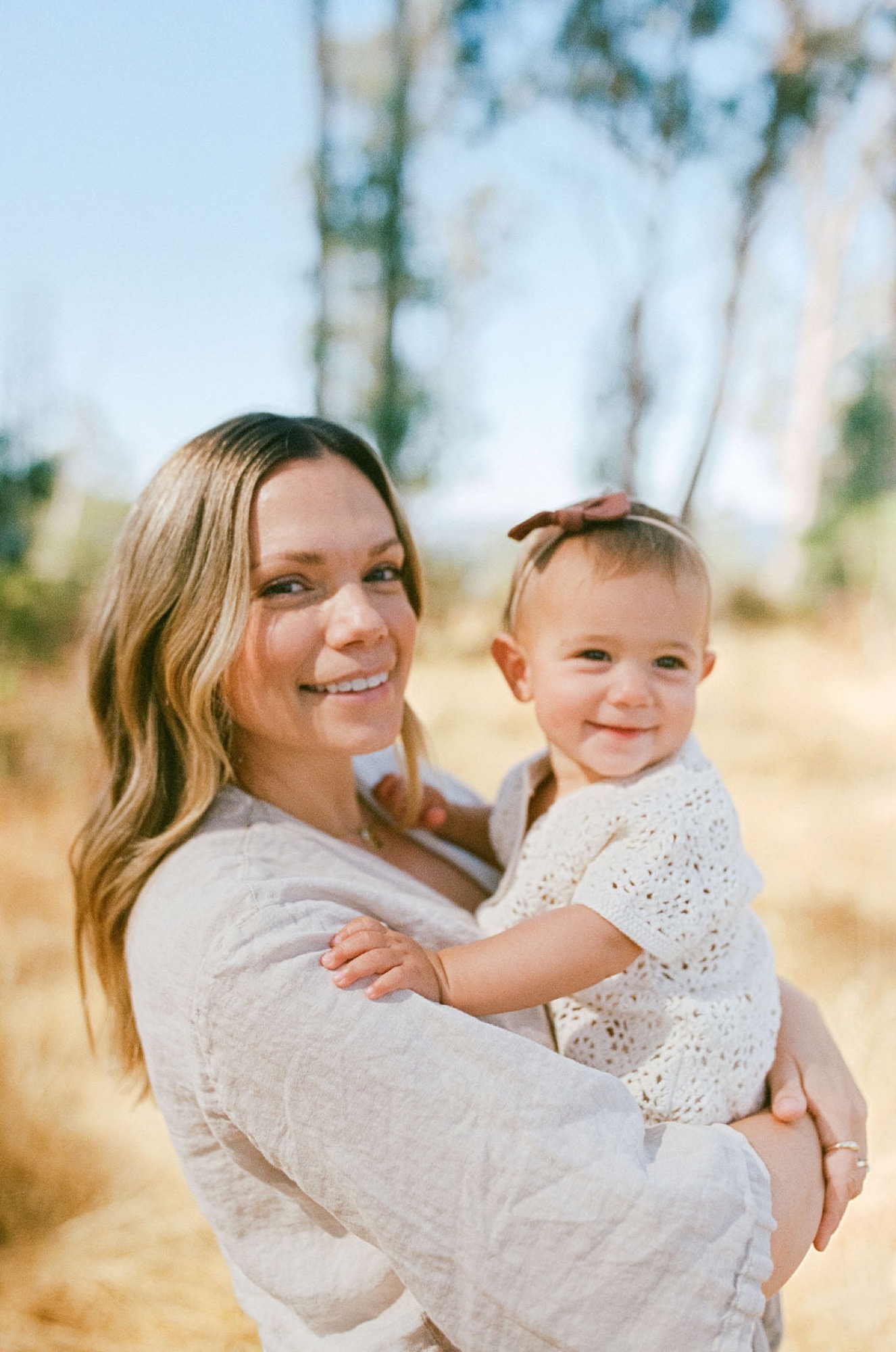 Mother and toddler share genuine smiles in golden afternoon light, wearing coordinated cream knit sweaters