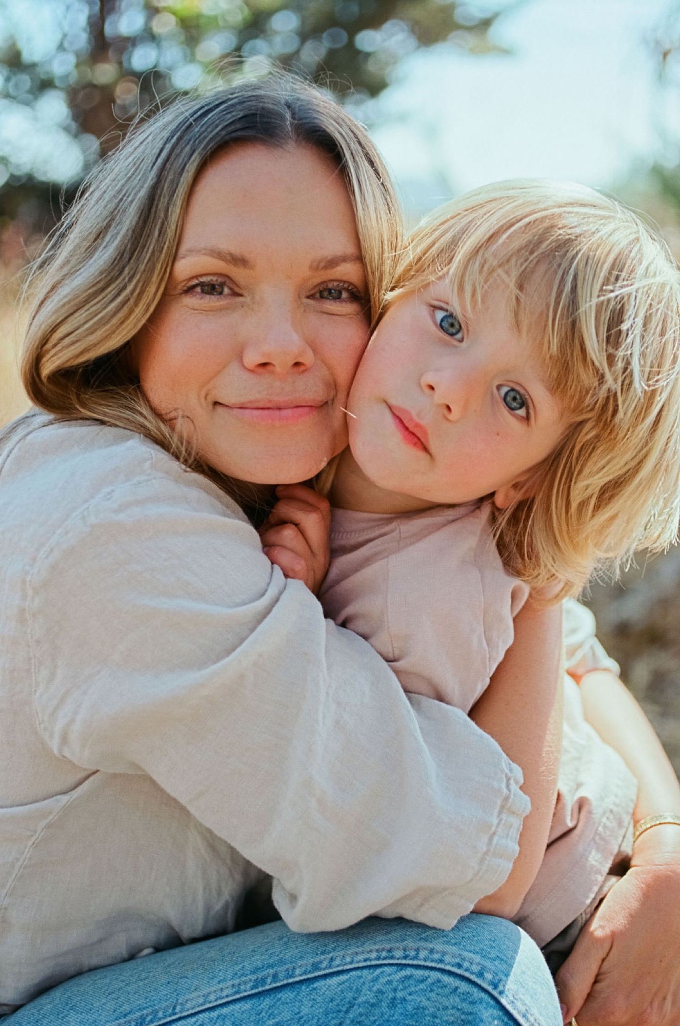 A mother and young child share a tender moment with warm, golden-hour light illuminating their gentle expressions and close embrace