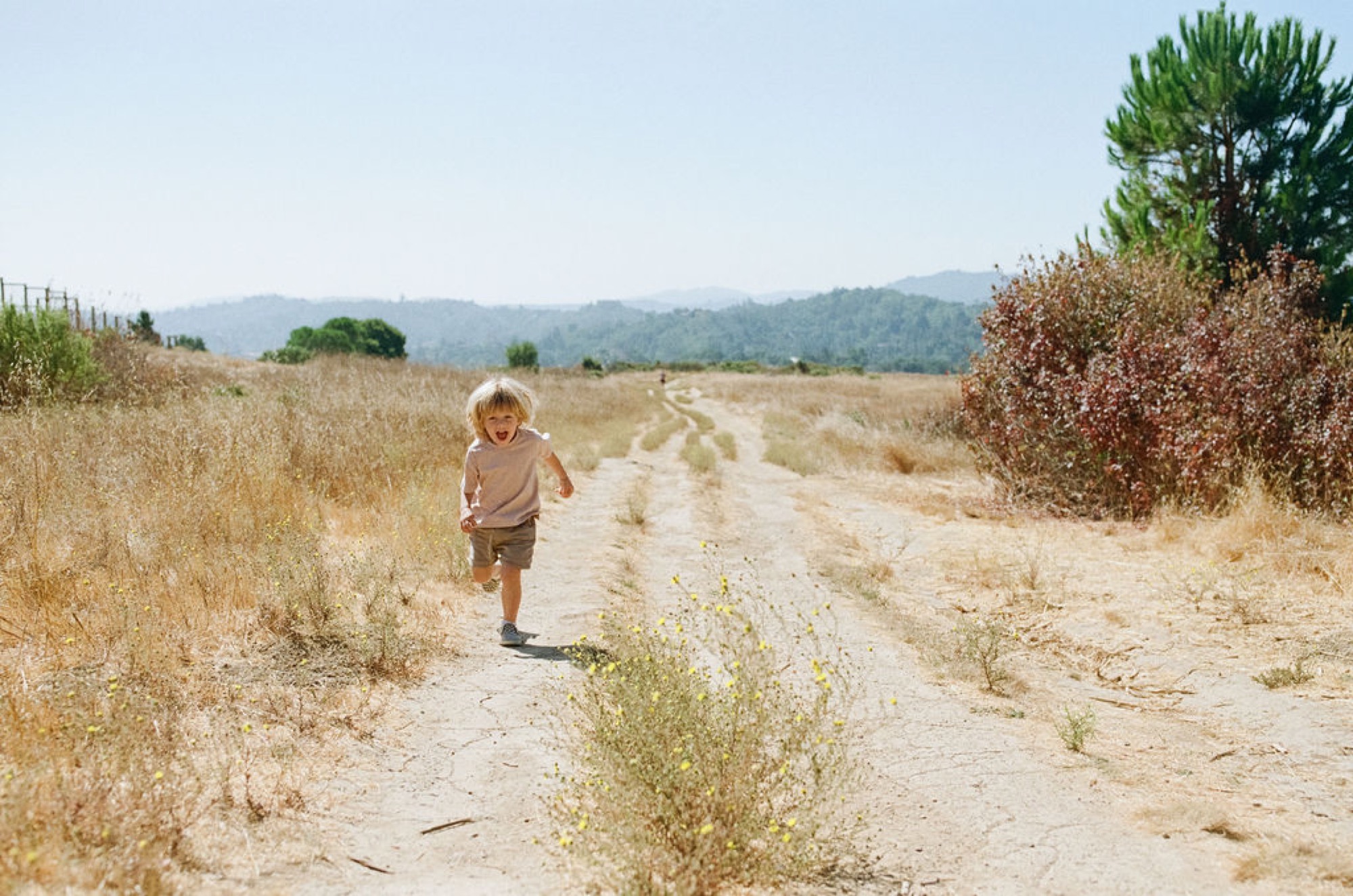 Blonde toddler running joyfully down a dusty trail in Marin County, candid lifestyle family photography