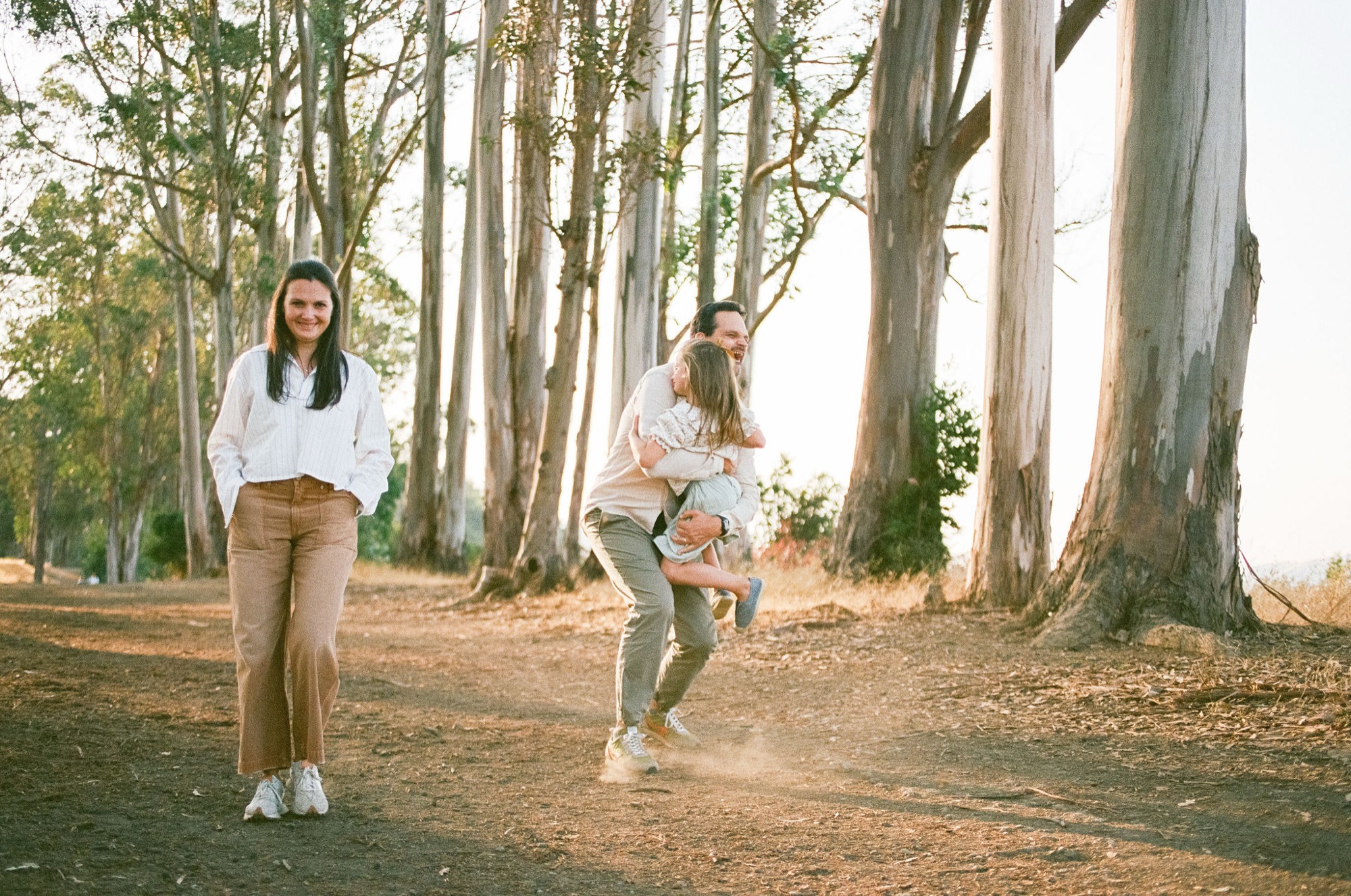 Two children run joyfully down a sun-dappled eucalyptus grove path, their movement and laughter captured mid-stride