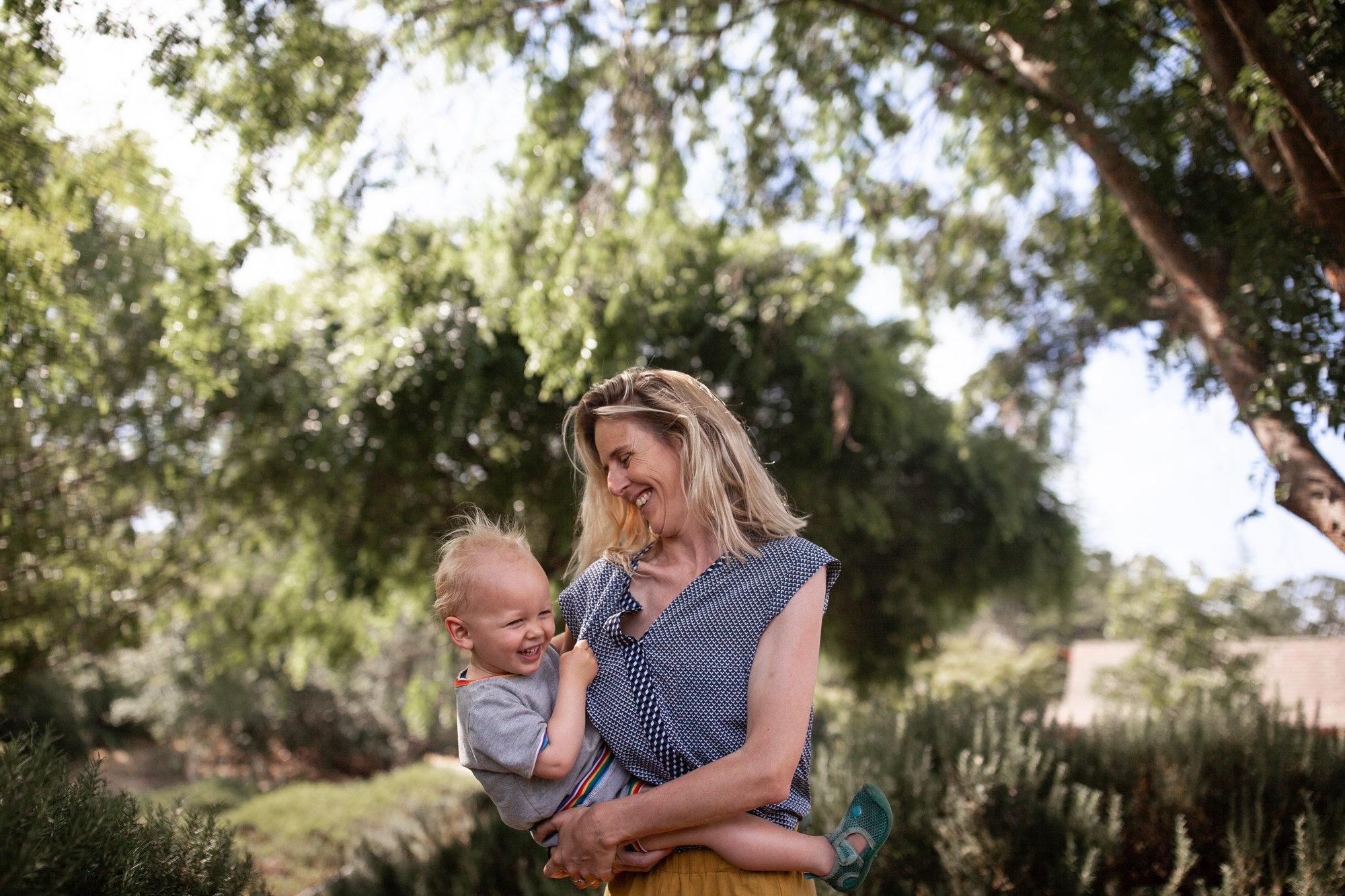 Mother laughing warmly with her toddler under towering trees at a park in Terra Linda, San Rafael