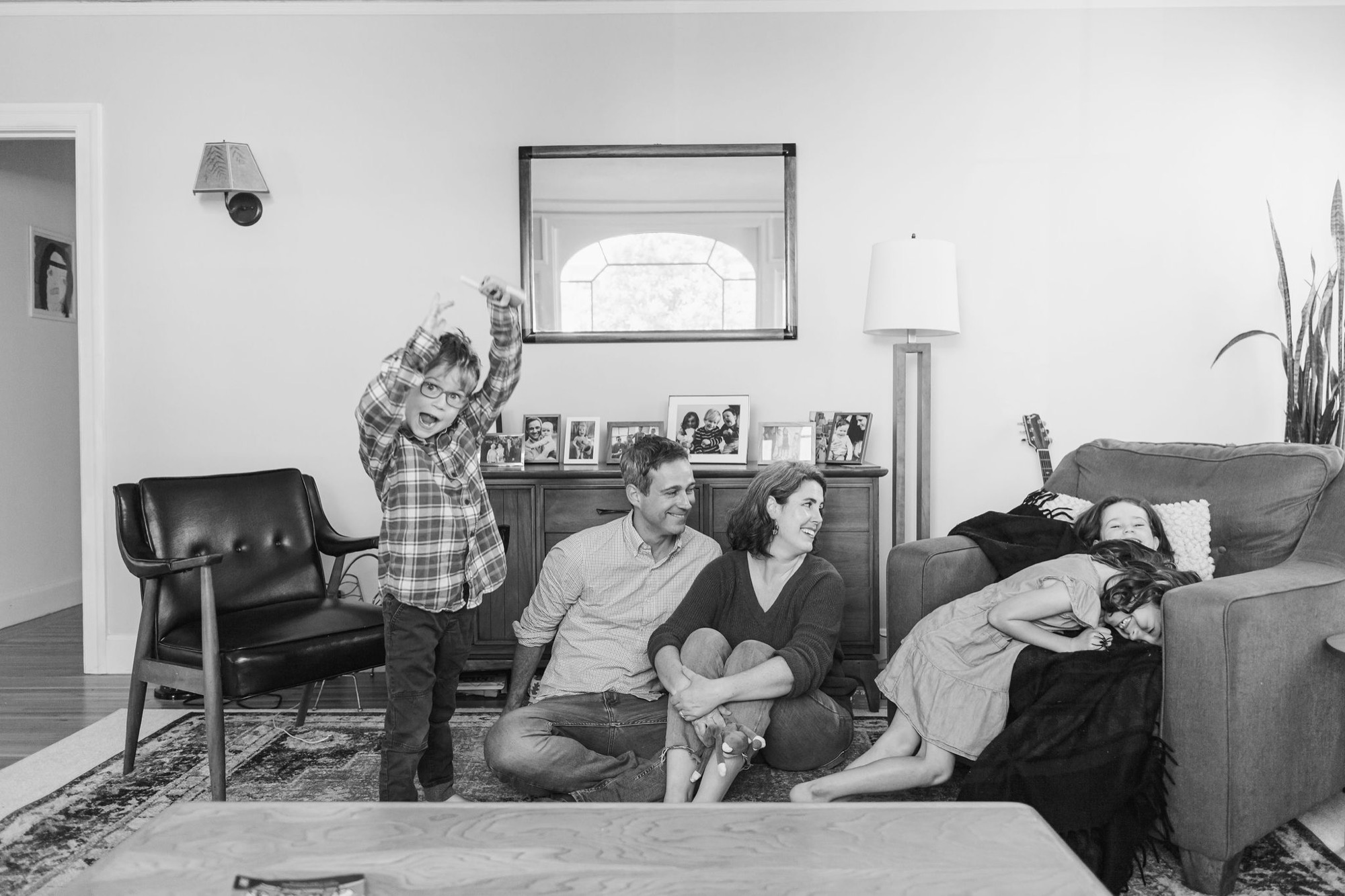 A family of five shares genuine laughter in their living room, with two children playfully positioned while parents sit contentedly on the floor beside an occupied sofa