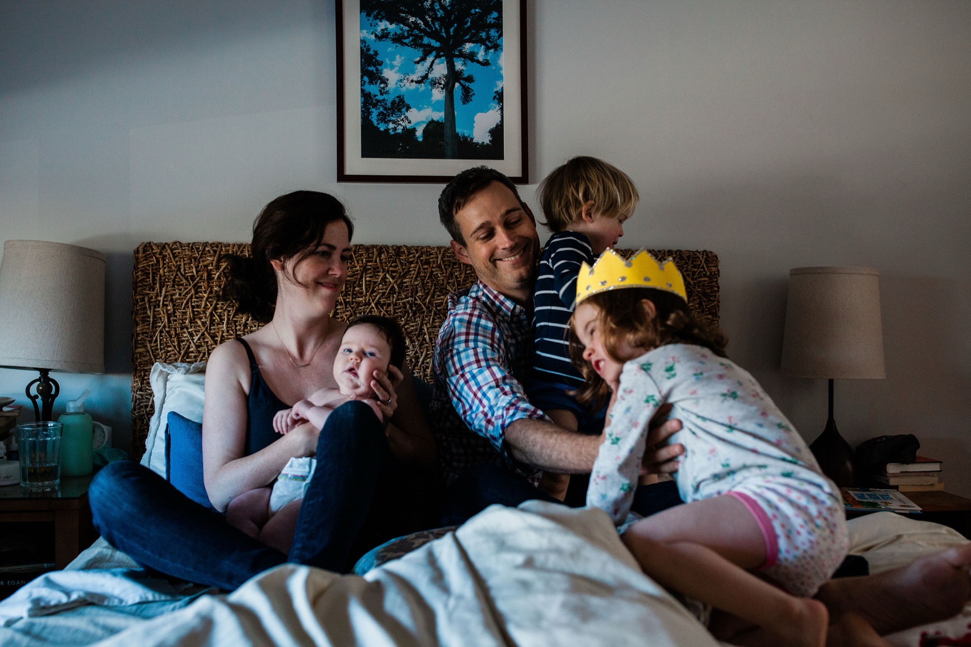 A family of five shares joyful laughter on a textured sofa, their genuine smiles and relaxed postures bathed in soft natural light
