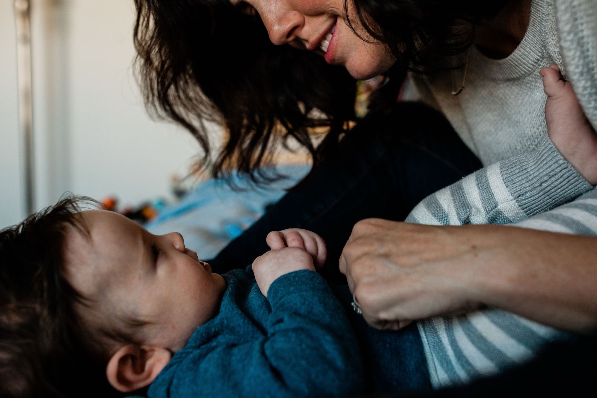 A mother gazes down tenderly at her infant son, who reaches toward her face with tiny hands in a intimate moment of connection