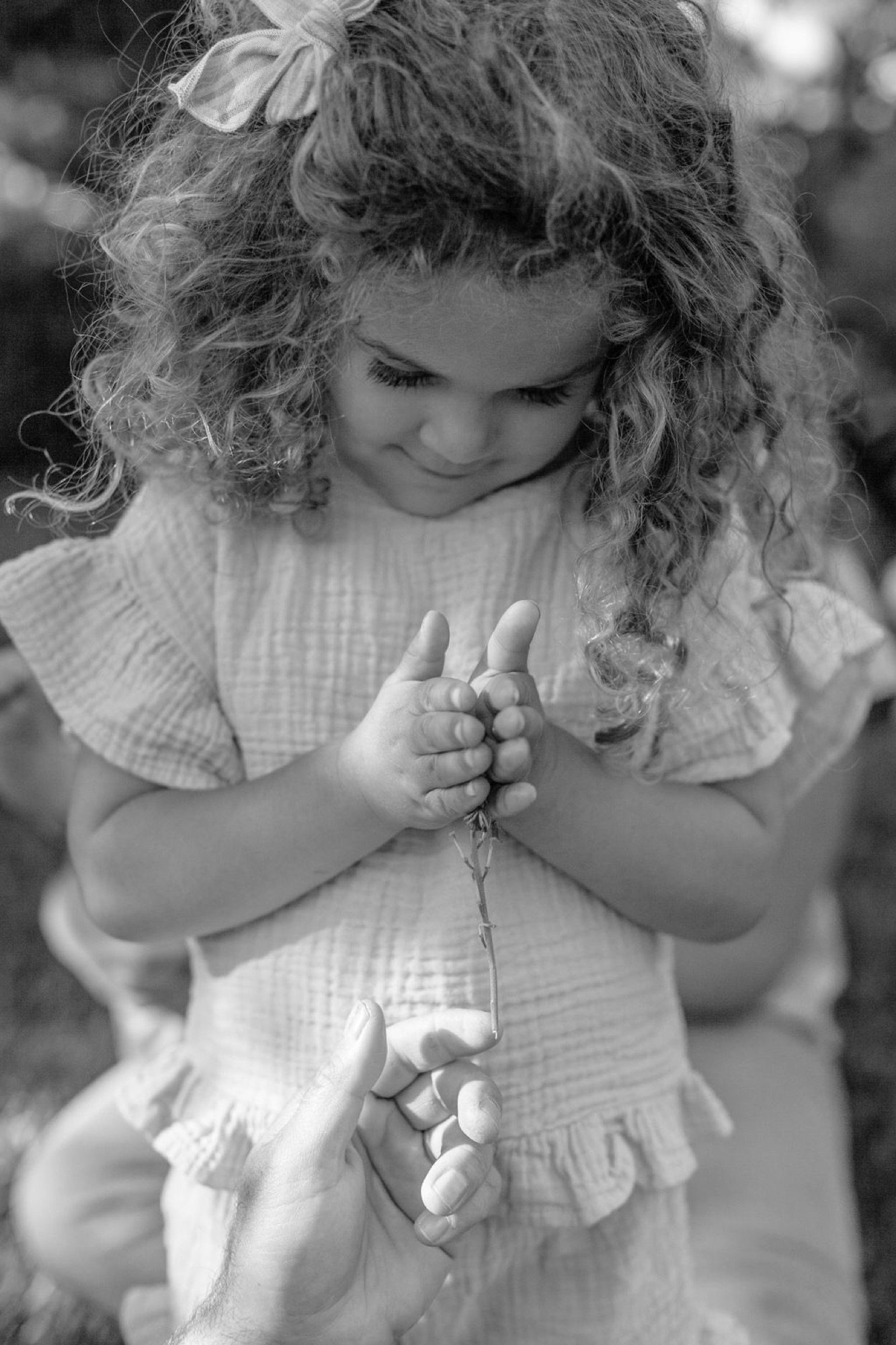 A young girl with curly hair gazes downward at a delicate flower stem held gently between her small hands