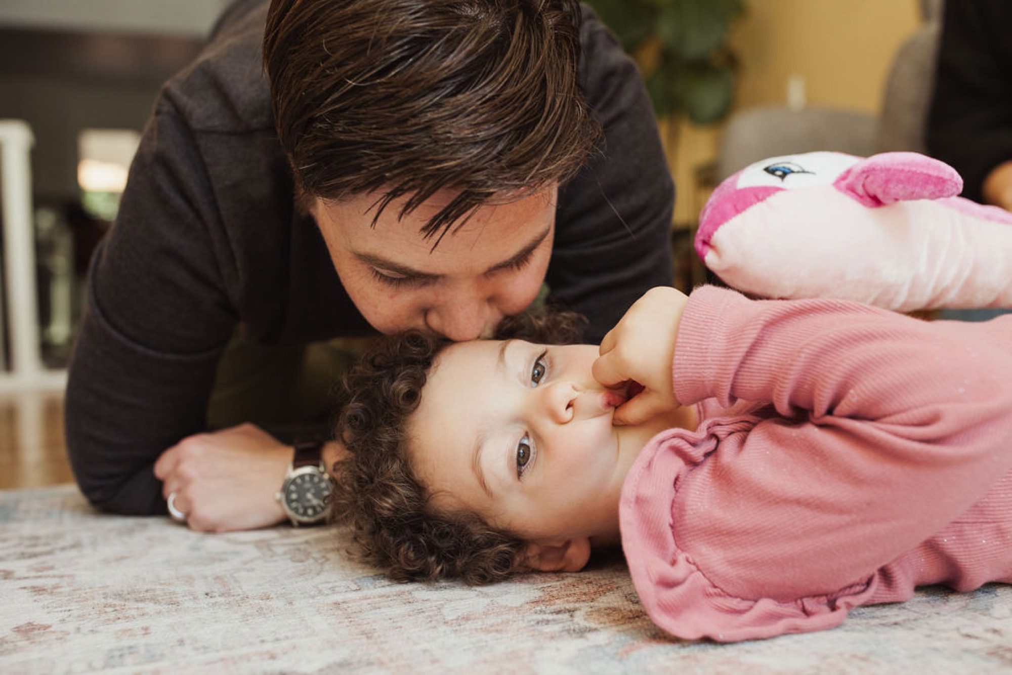 Father leans down to kiss his toddler daughter lying on the floor, both gazing at each other with genuine affection and joy