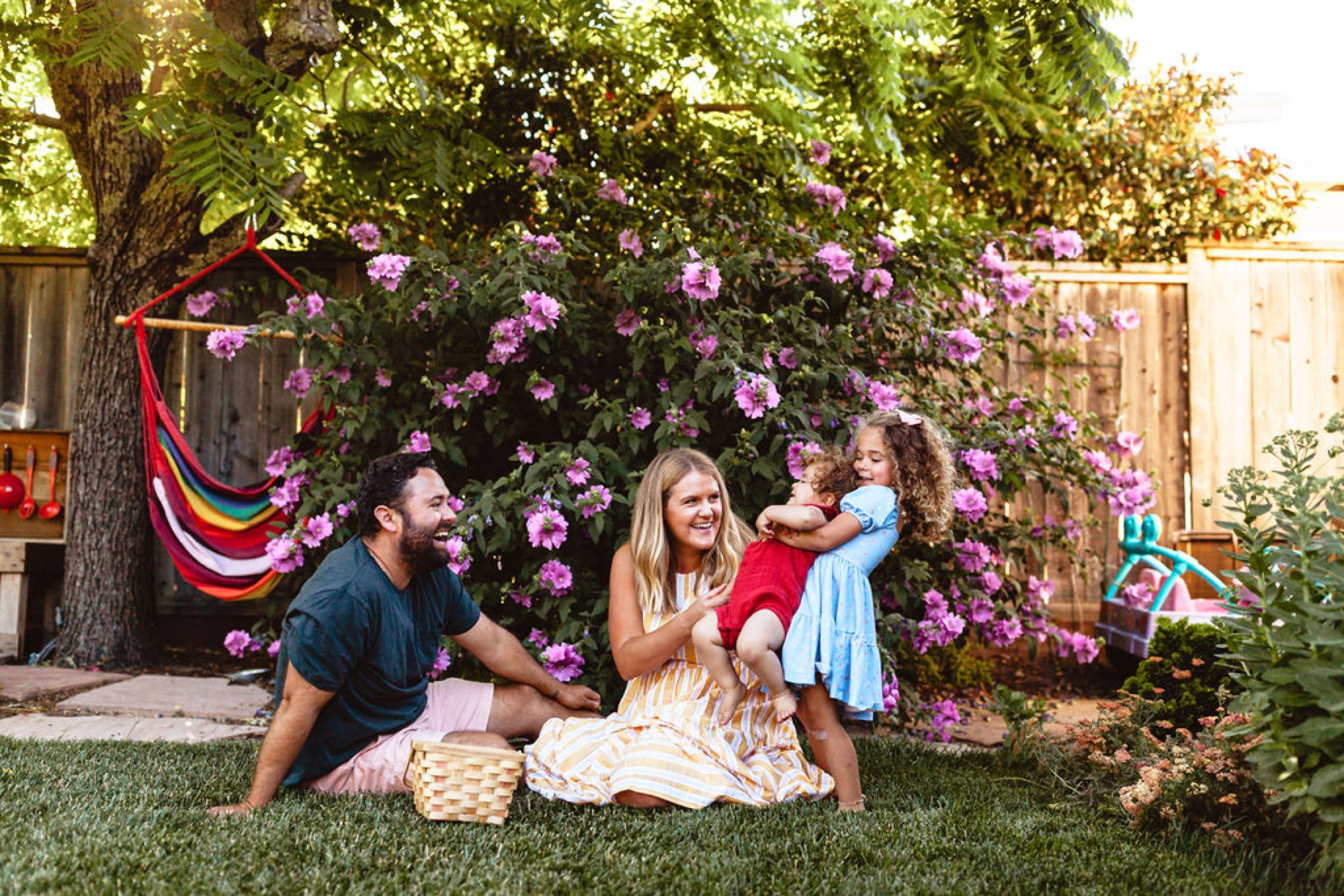 A family of four laughs together on the grass beneath a flowering tree in their San Rafael backyard