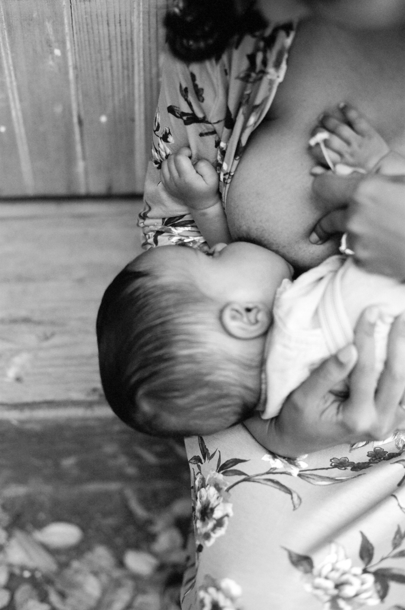 A mother holds her infant close while an older child reaches toward the baby's face in a tender moment of sibling connection
