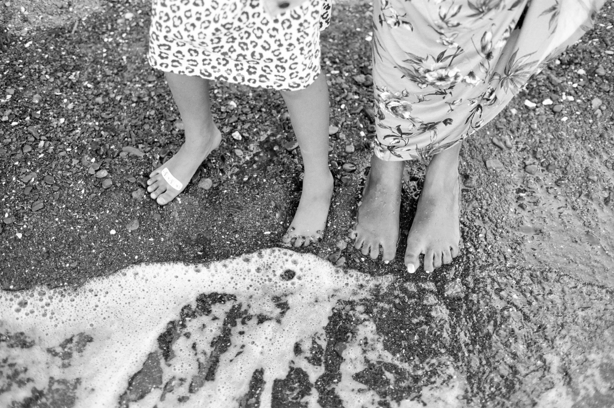Three barefoot children stand at the water's edge, their legs and feet wet from wading in the foamy surf