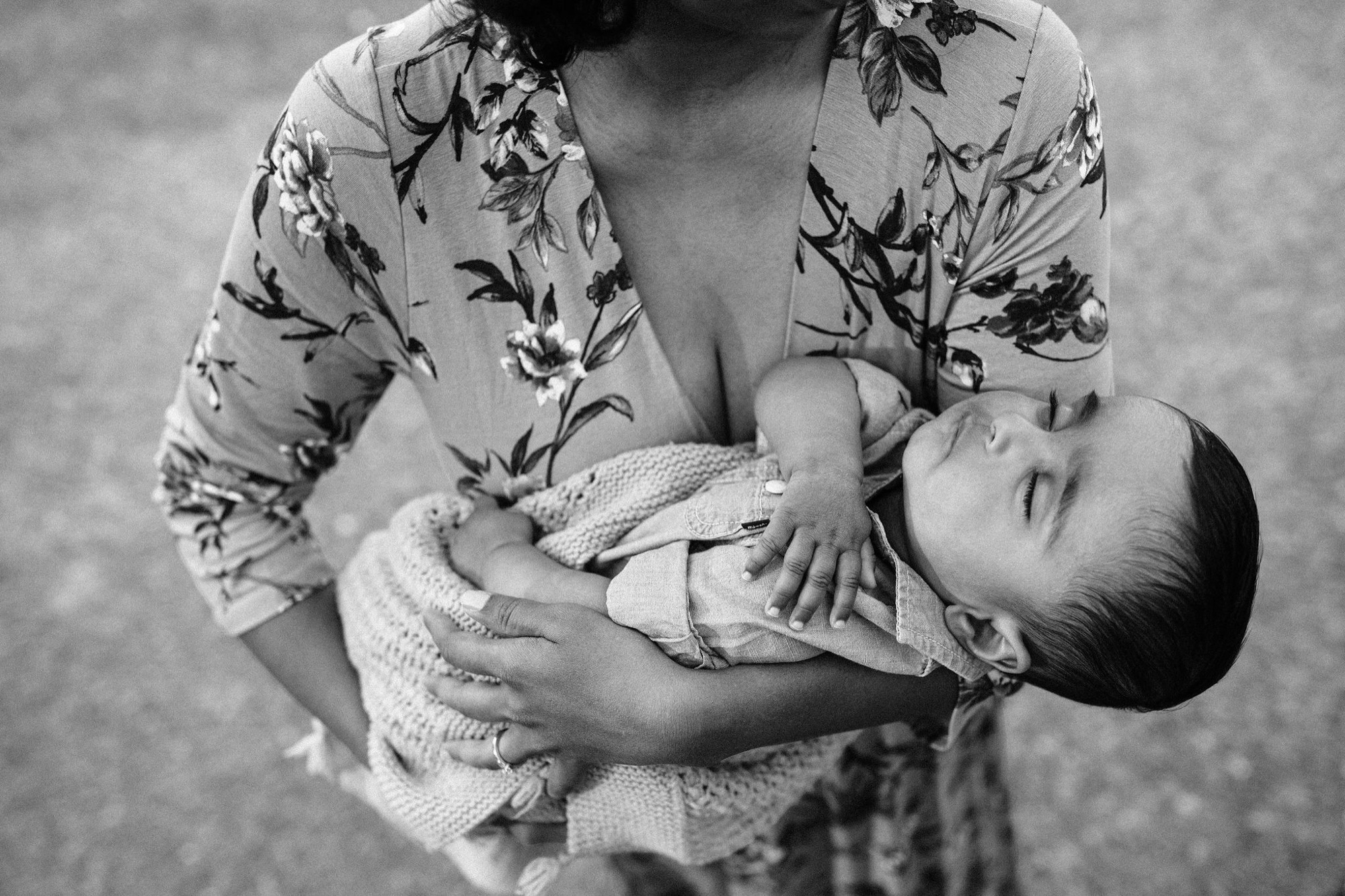 A mother in a floral print dress cradles her infant in her arms, gazing downward with tender affection against a soft, textured background