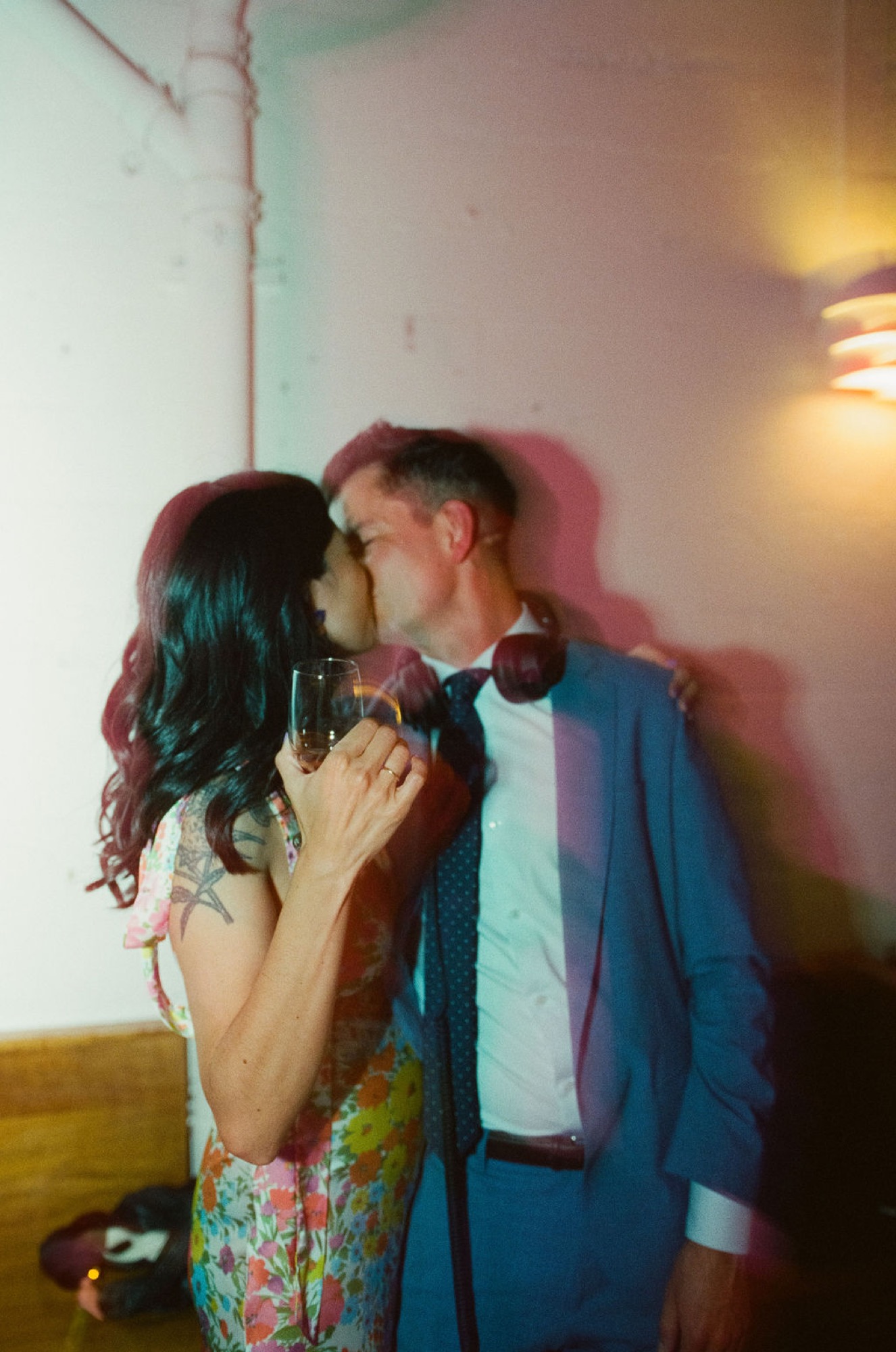 A couple shares an intimate moment in warm amber light, their silhouettes caught mid-kiss against a soft white wall