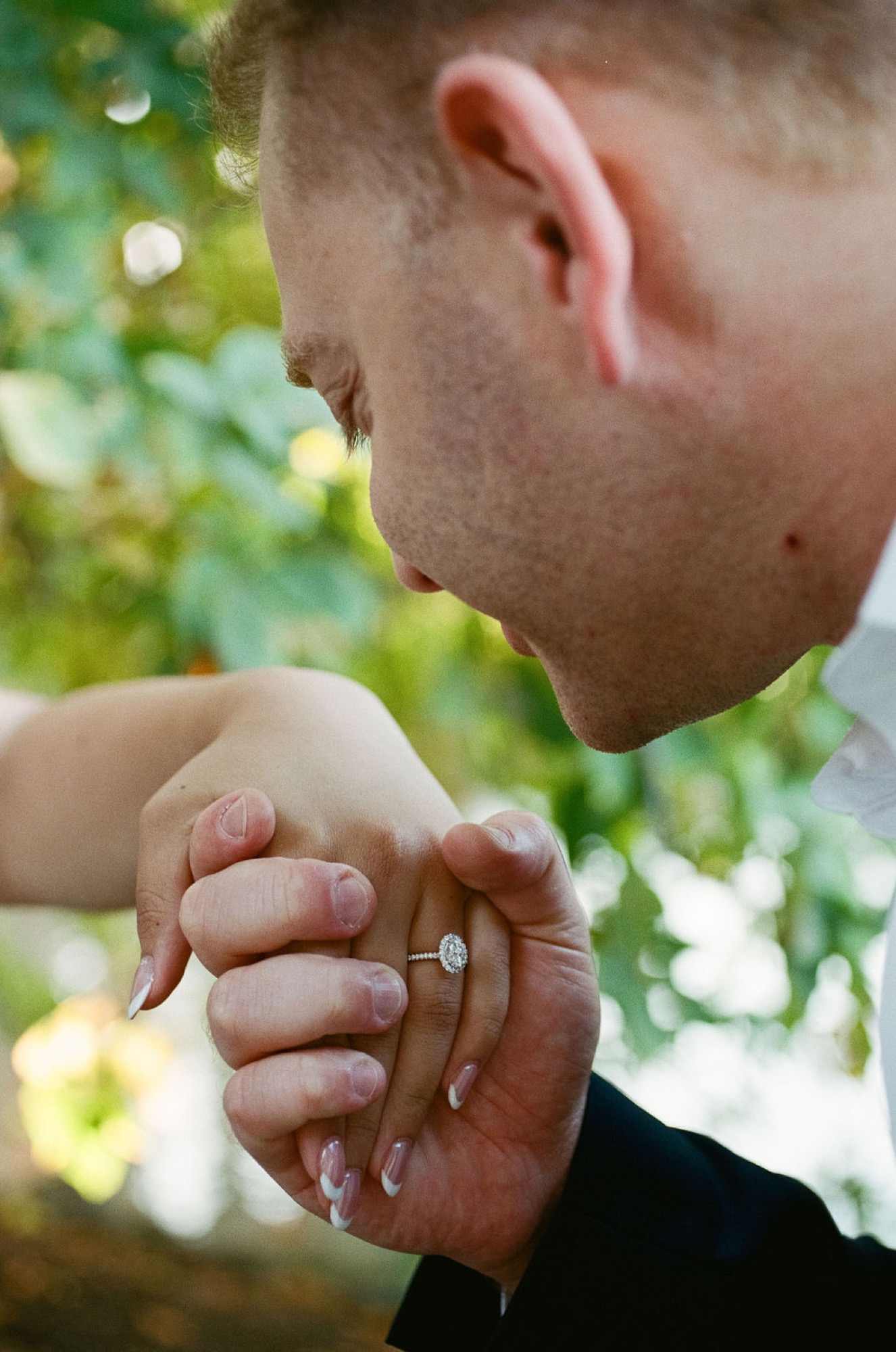 A man gazes downward while gently holding a child's small hand, displaying matching rings in dappled sunlight