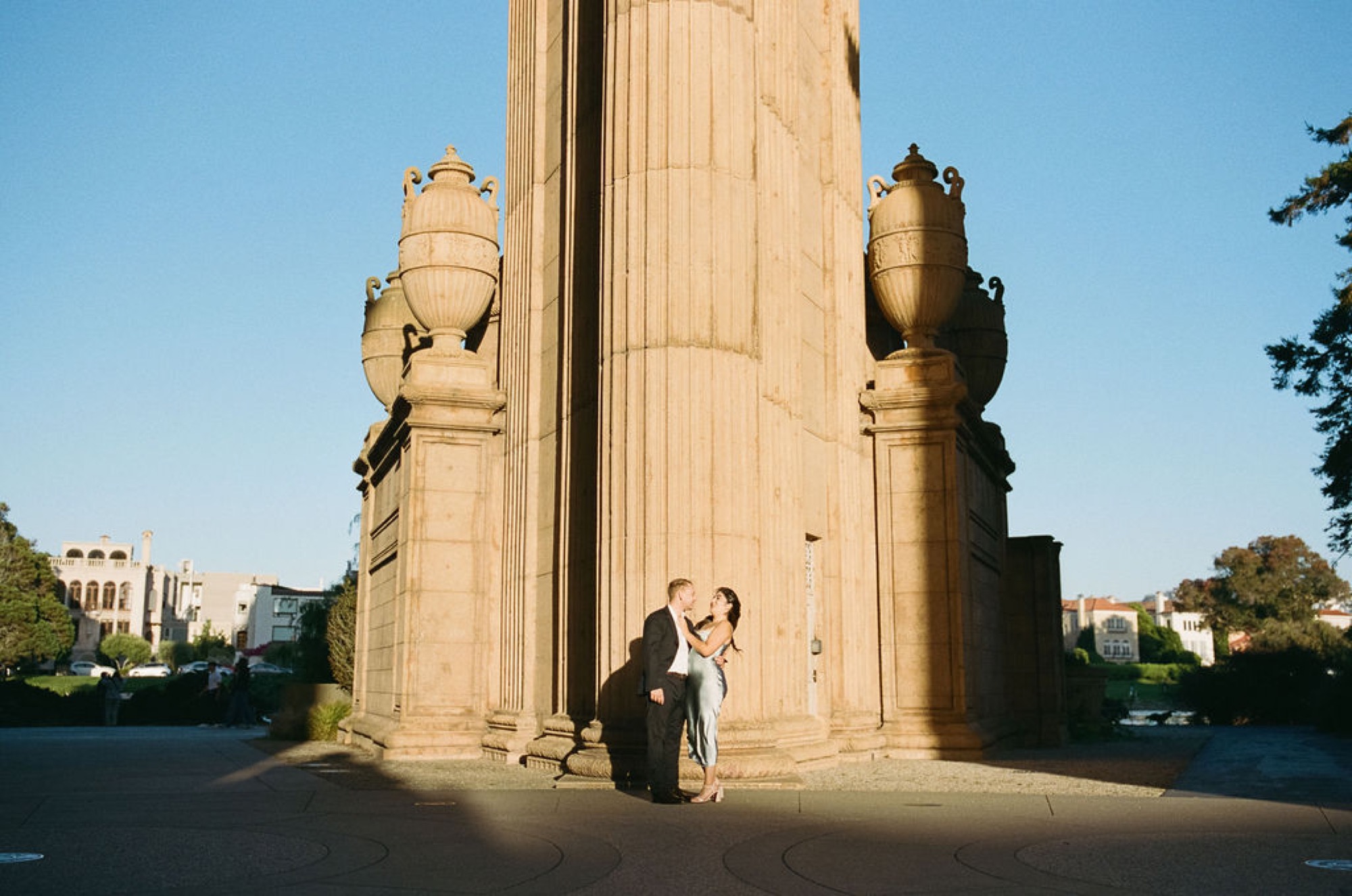 A woman in dark clothing sits contemplatively beneath towering stone columns, bathed in golden afternoon light at the Palace of Fine Arts