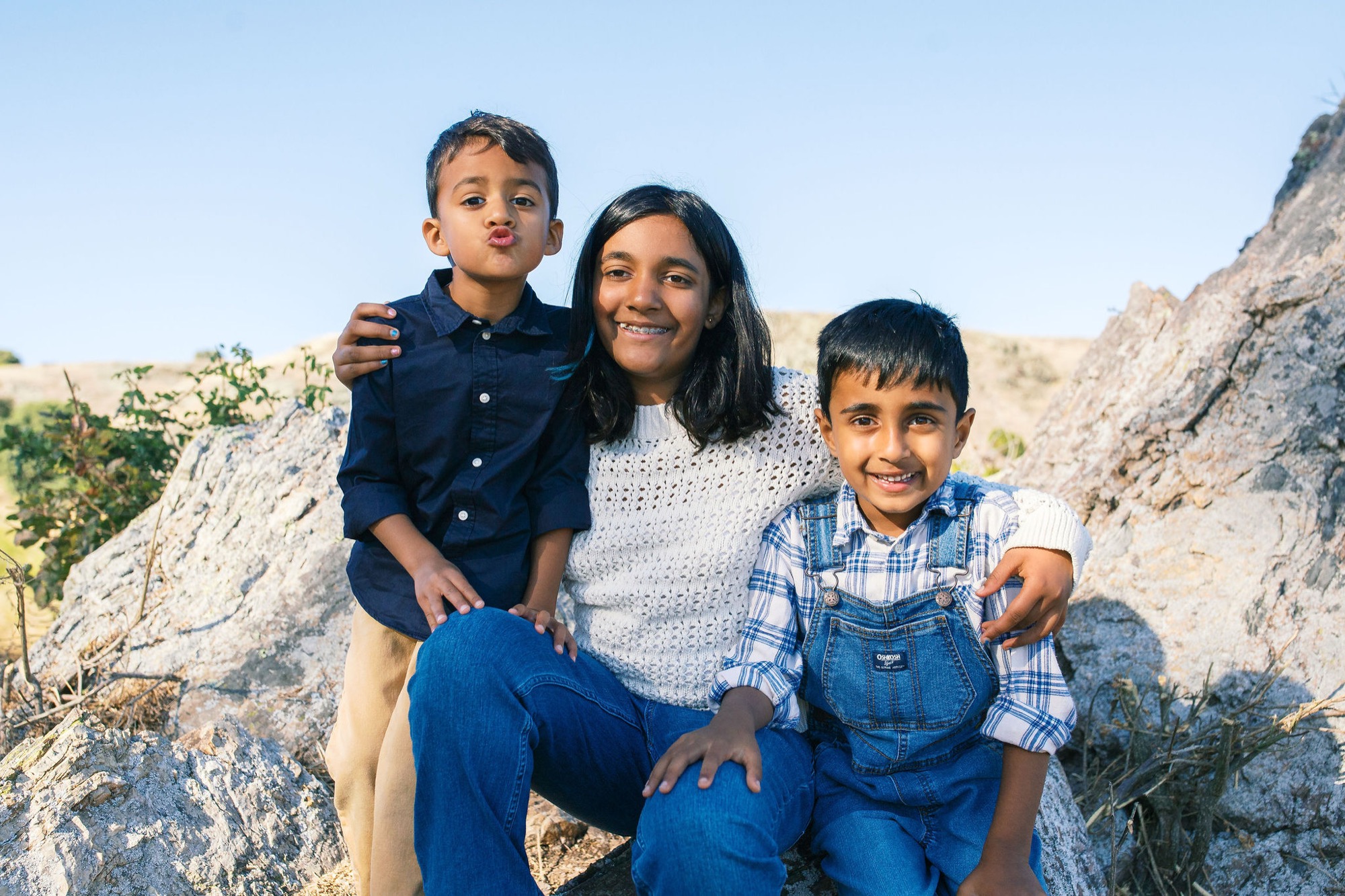 Marin family photographer captures a mom and her two boys laughing and playing on sun-warmed boulders in the Marin County hills — one little one hamming it up with a pouty face while his brother grins ear to ear, a perfectly imperfect family portrait full of personality and love.