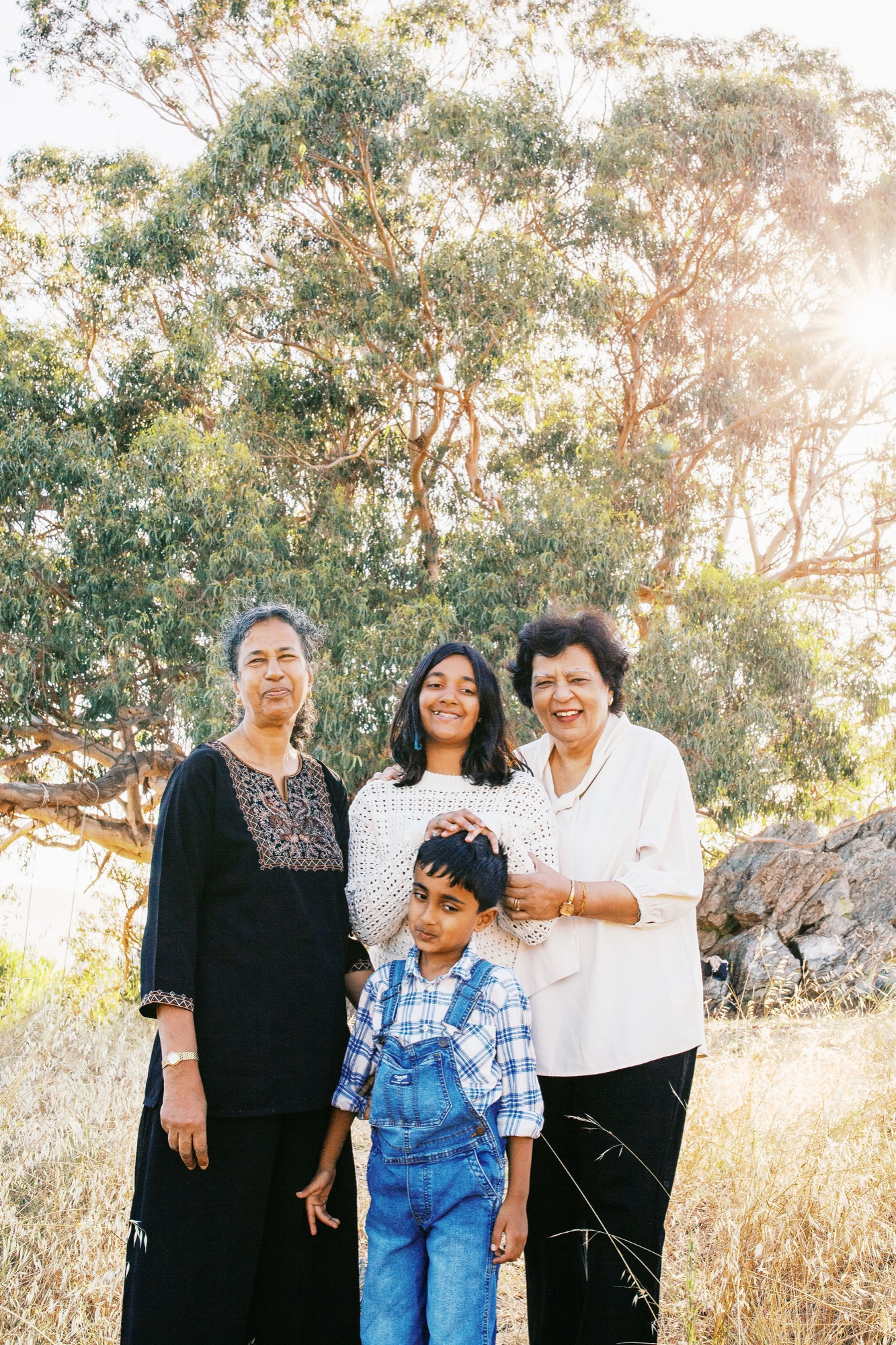 Four generations stand together among golden eucalyptus trees, with warm afternoon light filtering through the canopy behind them