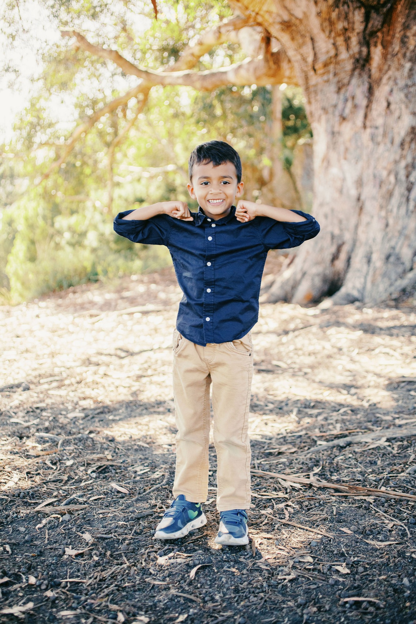 Marin family photographer captures a little boy showing off his muscles with the biggest smile under a sprawling oak tree during an outdoor mini session in Marin County — Bay Area children's and family photography.
